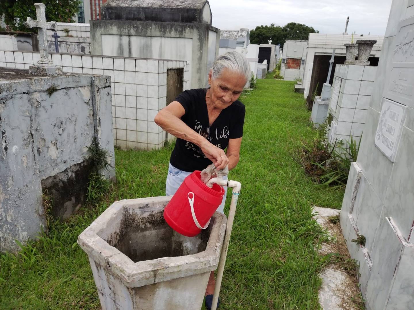 Doña Ligia Ramírez recoge agua para ir a limpiar la tumba en donde está su esposo en el cementerio Obreros