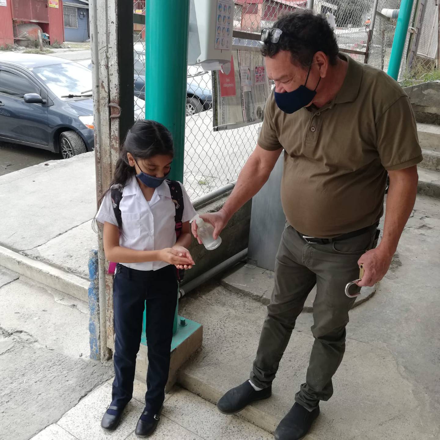 Malori Pérez Calderón recibe alcohol en gel a la entrada de la escuela Ismael Coto de Alajuelita de parte de Édgar Acuña