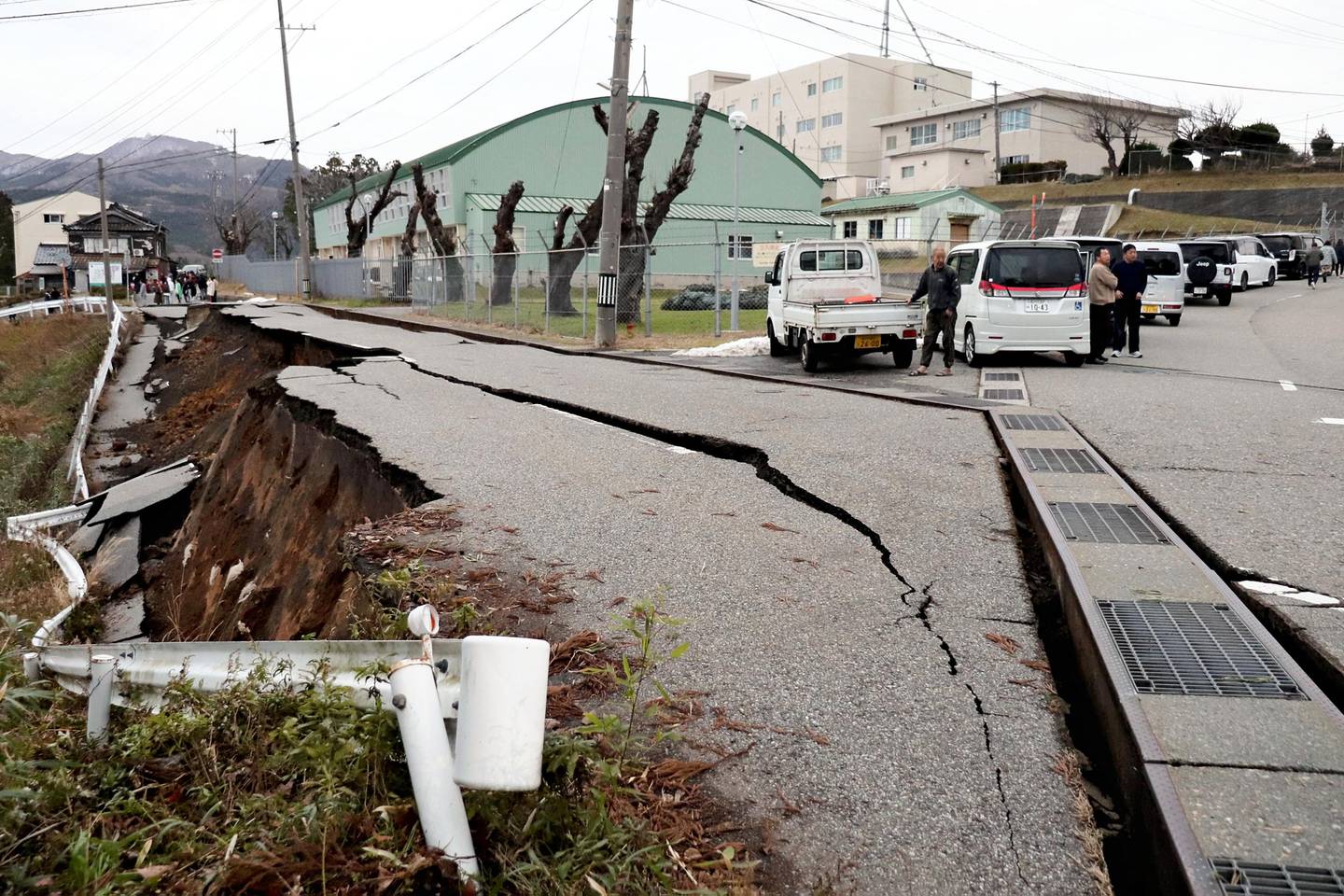 People stand next to large cracks in the pavement after evacuating into a street in the city of Wajima, Ishikawa prefecture on January 1, 2024, after a major 7.5 magnitude earthquake struck the Noto region in Ishikawa prefecture in the afternoon. Tsunami waves over a metre high hit central Japan on January 1 after a series of powerful earthquakes that damaged homes, closed highways and prompted authorities to urge people to run to higher ground. (Photo by Yusuke FUKUHARA / Yomiuri Shimbun / AFP) / Japan OUT / NO ARCHIVES - MANDATORY CREDIT: Yomiuri Shimbun