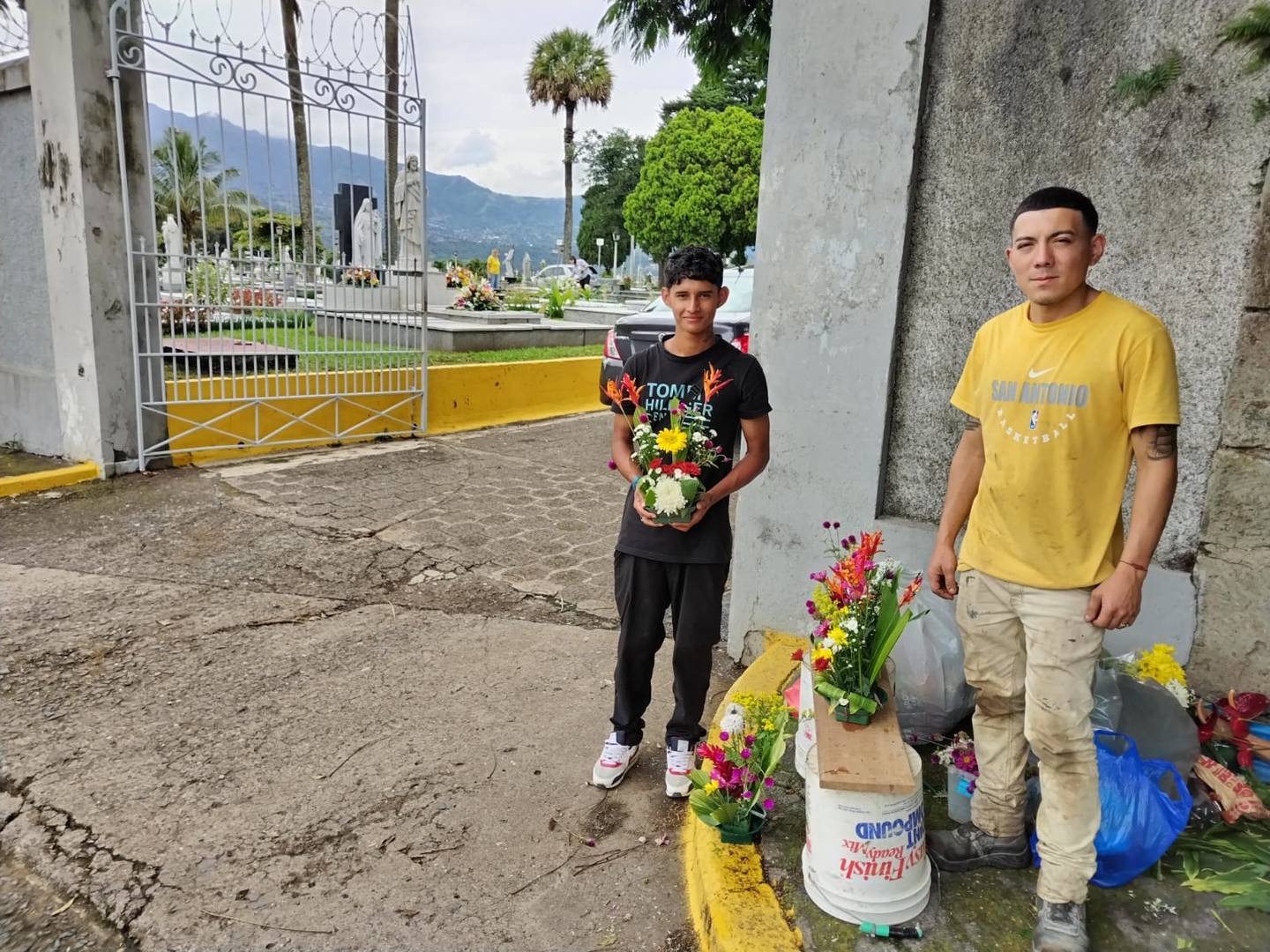 Juan Carlos Gutiérrez (negro)y Josué Román, venden flores en una de las entradas del cementerio General en San José
