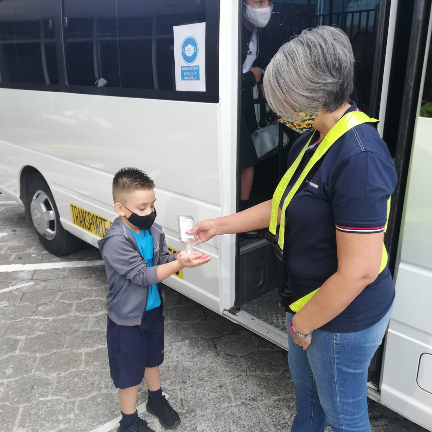 Shirley Miranda Núñez, quien transportará estudiantes en su microbus, le da alcohol en gel a Josué Alfaro Sánchez, quien irá al kinder en esa micro.