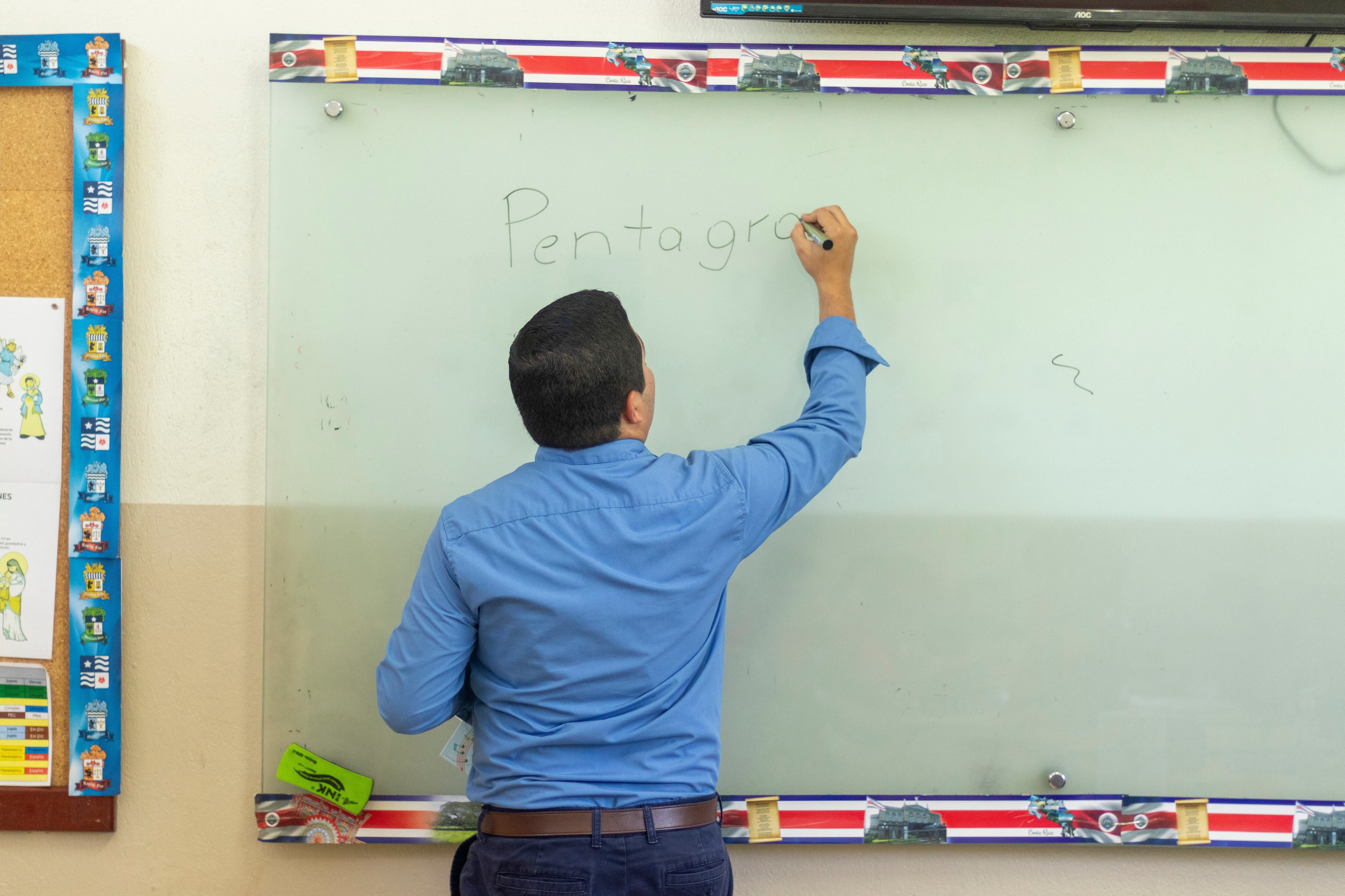 En la imagen un profesor escribiendo en una pizarra