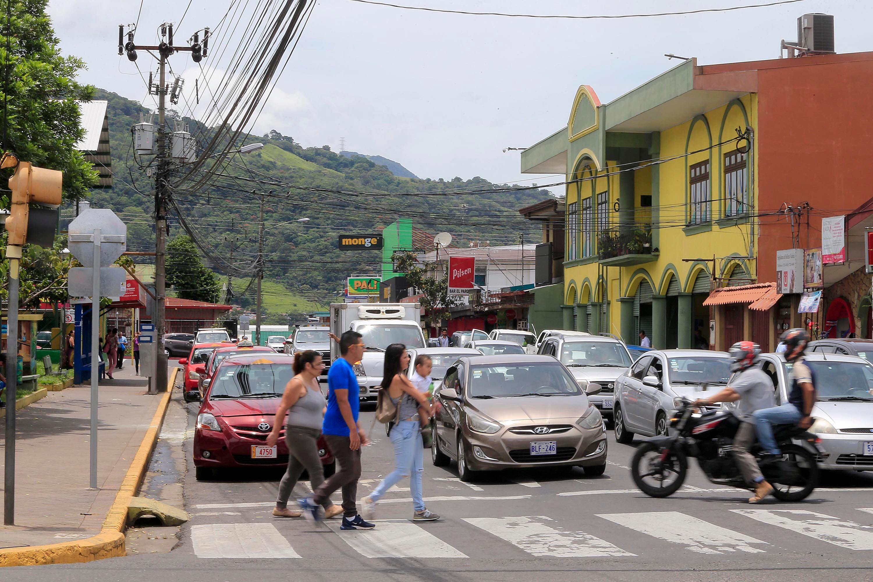 Cruce peatonal en el centro de Alajuelita, con vehículos y personas cruzando la calle, ilustrando el cantón con mayor crecimiento en ejecución presupuestaria en 2023.
