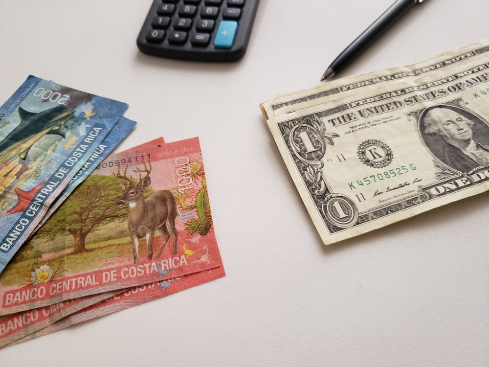 Billetes de colones costarricenses y dólares estadounidenses junto a una calculadora y un bolígrafo, simbolizando las proyecciones del crédito en diferentes monedas en Costa Rica para 2025.