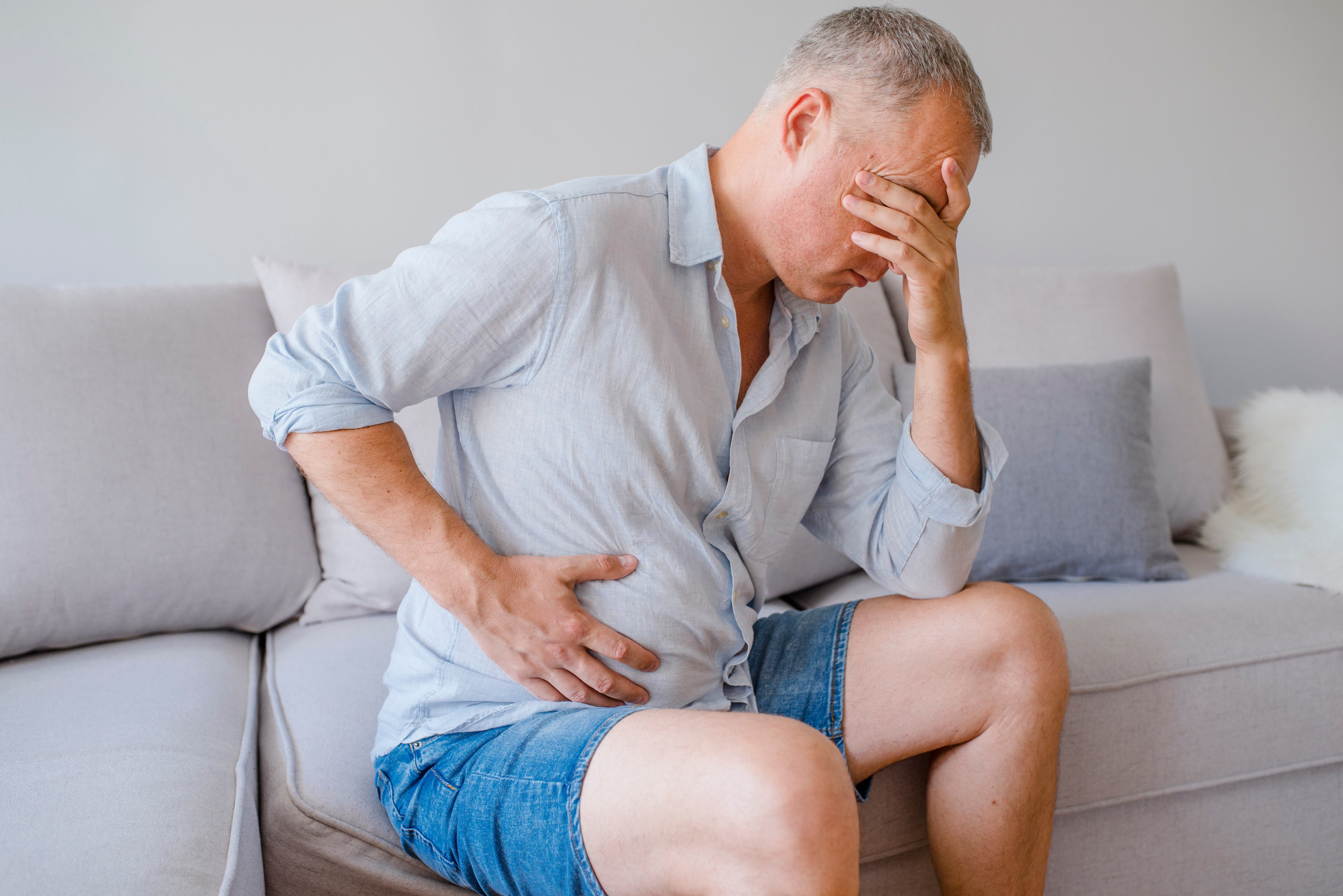 Hand of old man holding stomach suffering from pain, diarrhea, indigestive problem. A middle-aged man has a stomach ache. Unhappy man suffering from stomach ache at home