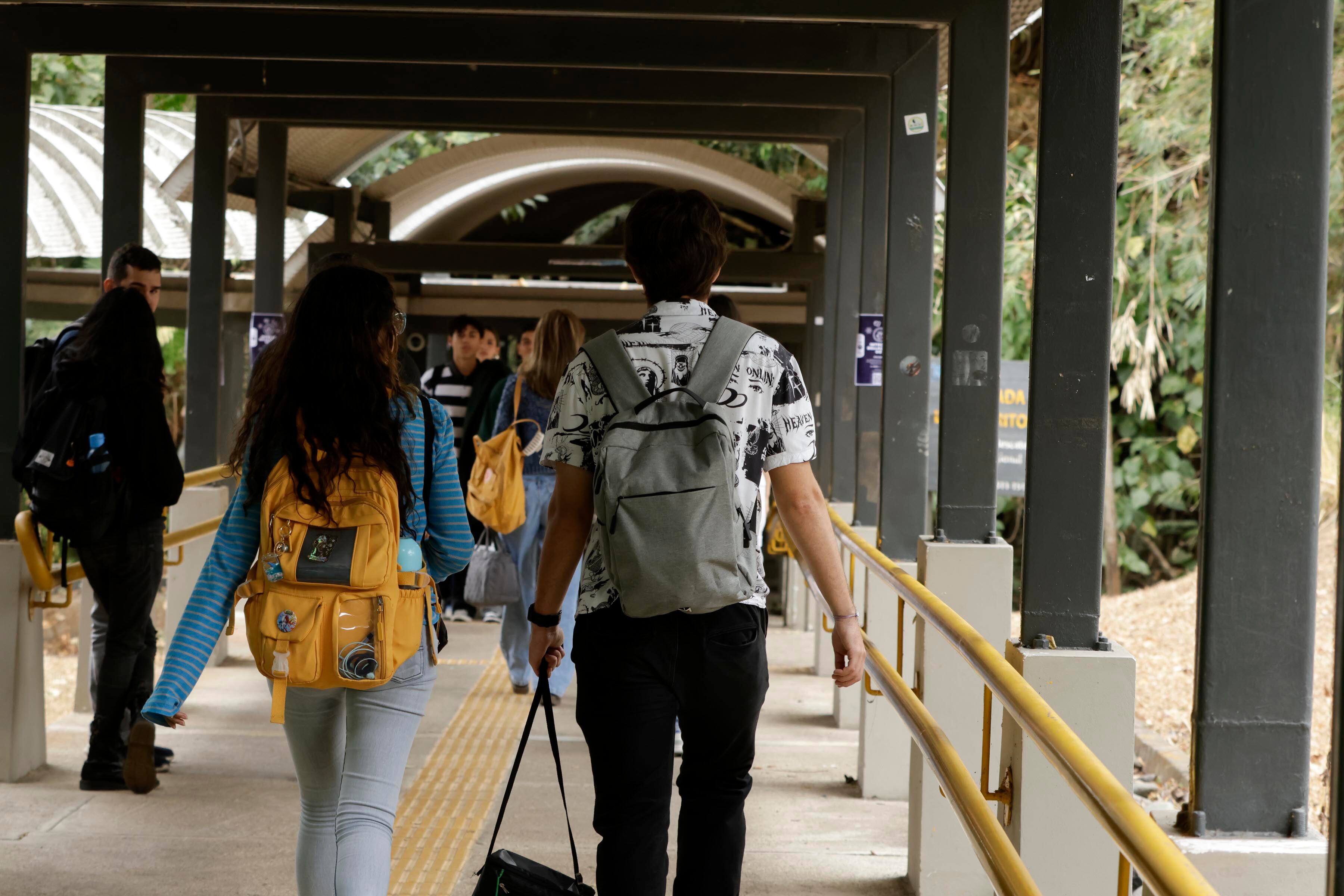 Un pasillo al aire libre, estudiantes universitarios caminando de espaldas.