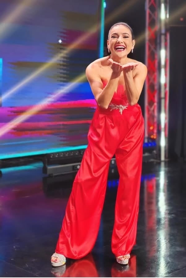 Foto de Nancy Dobles enviando un beso, usa un traje de color rojo.