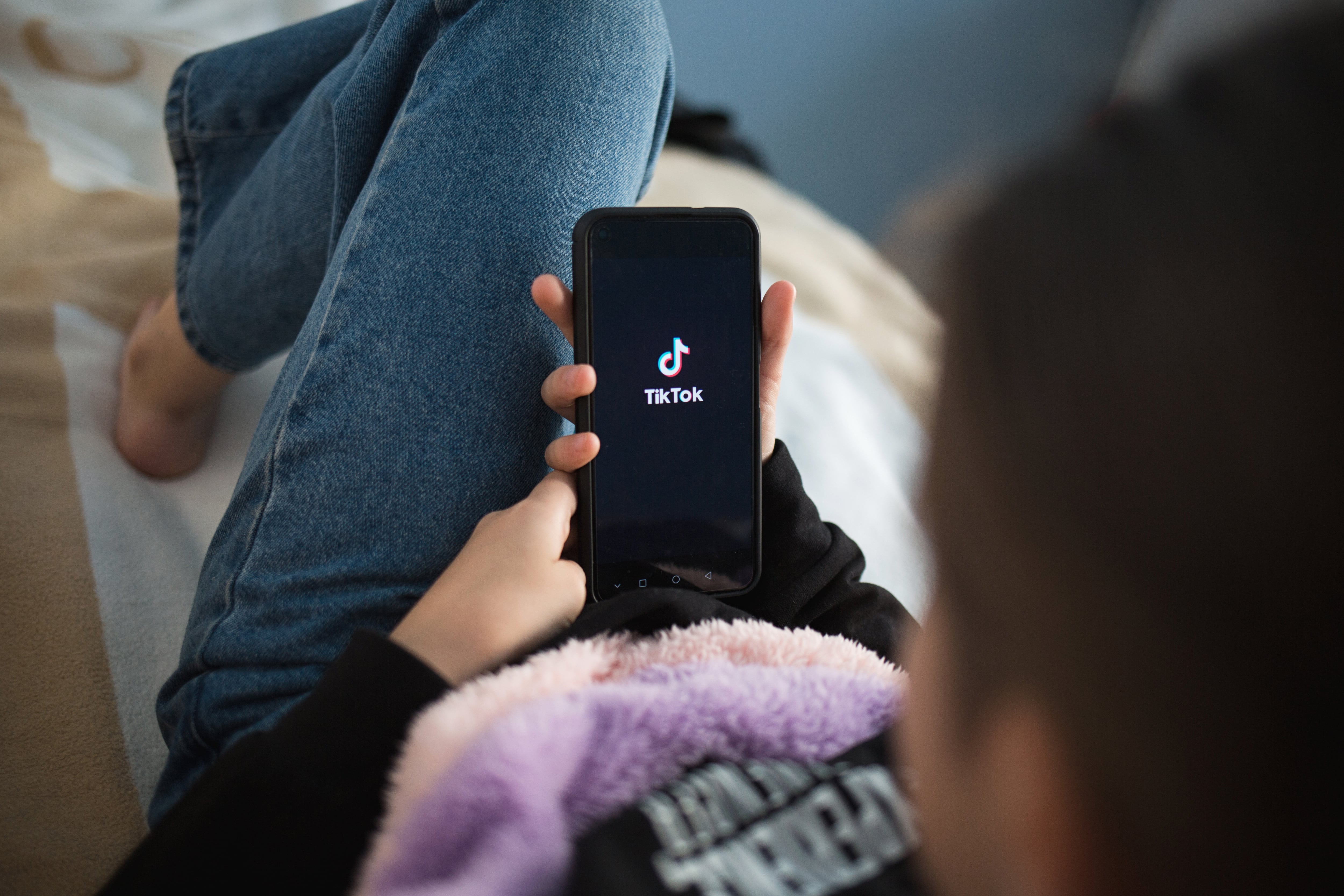 Joven adolescente recostado recostada con su celular viendo TikTok