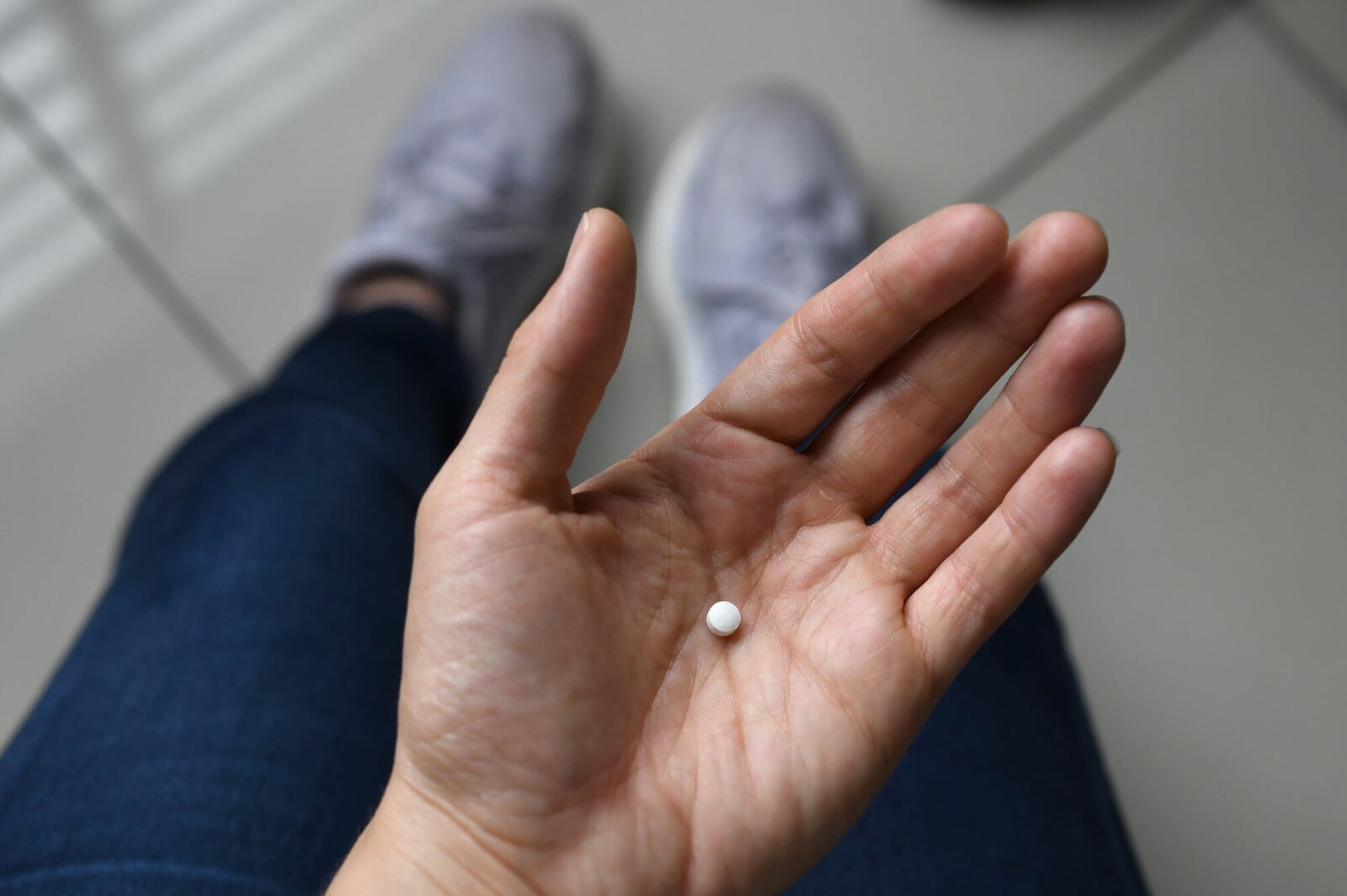 Una mano sostiene una pequeña píldora de color blanco.