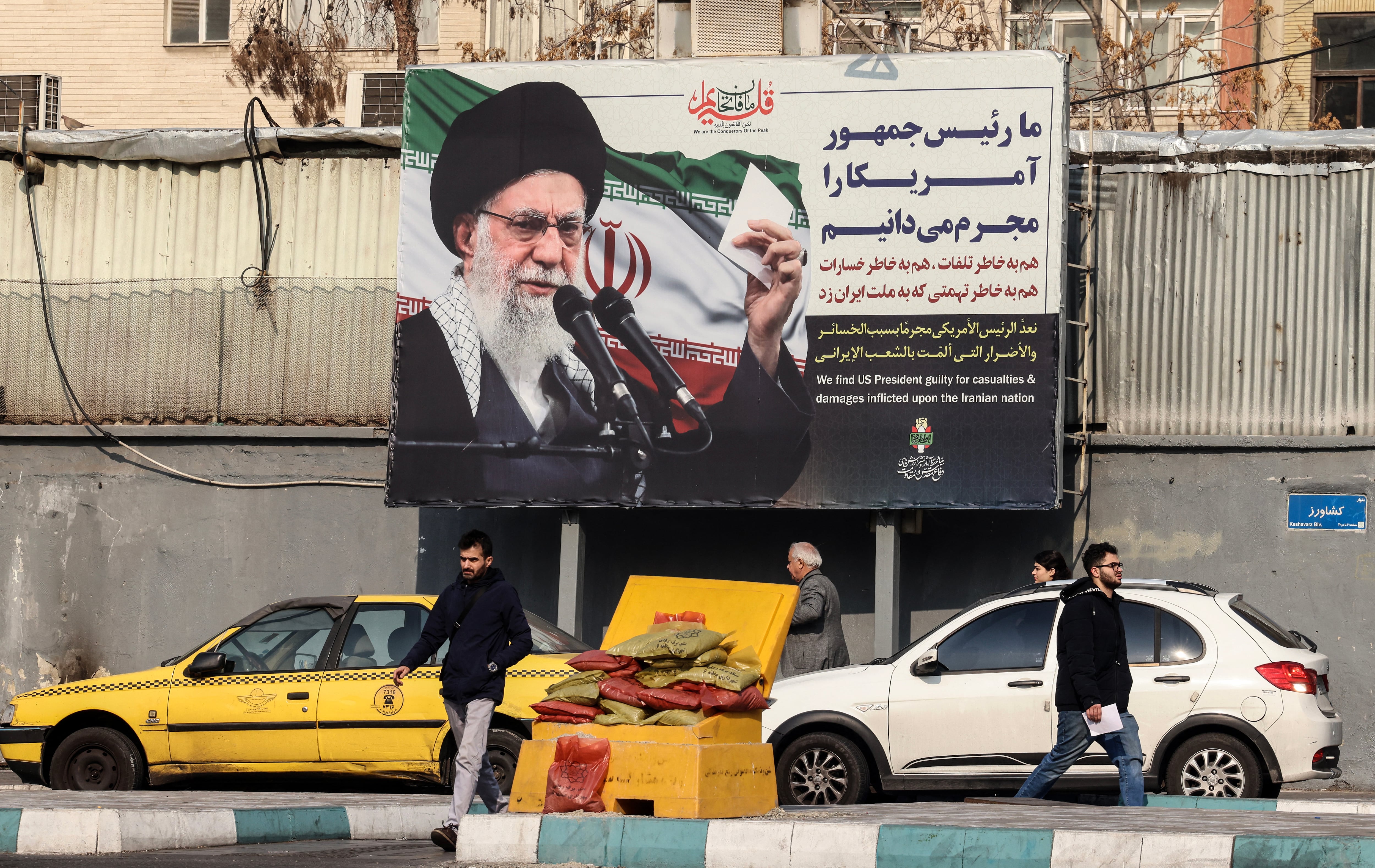 Iranians walk past a billboard showing Iranian supreme leader Ayatollah Ali Khamenei with anti-US rhetoric in Tehran on January 27, 2026. A US naval strike group led by an aircraft carrier has deployed to Middle Eastern waters, the United States said on January 26, 2026, as Tehran warned it was ready to hit back at any American attack launched in response to a crackdown on anti-government protests. (Photo by ATTA KENARE / AFP)