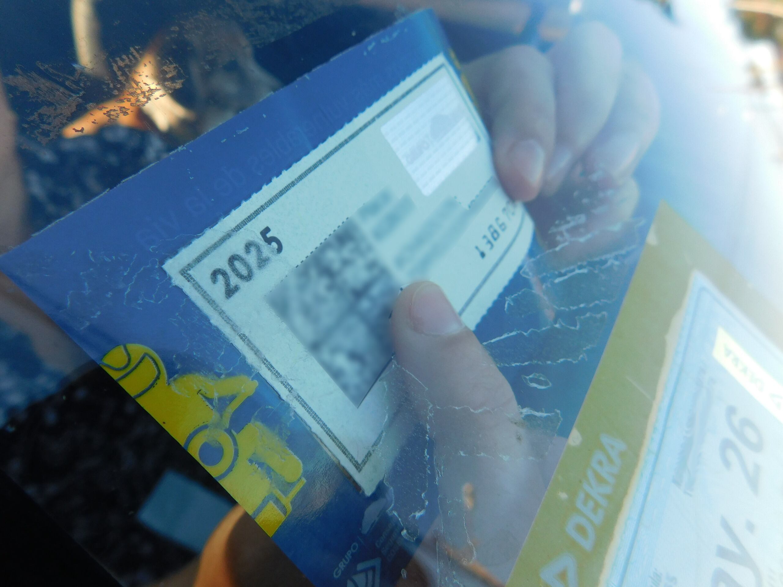 Una persona pega la calcomanía del marchamo del 2025 en el parabrisas de su vehículo.