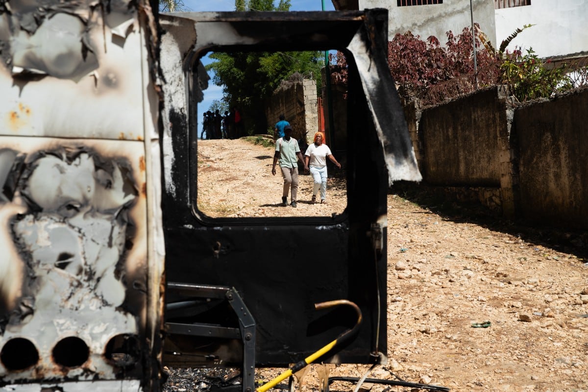 Personas caminan junto a los restos de un vehículo incendiado tras una noche de violencia en la que pandillas armadas mataron a más de 20 personas en Kenscoff, un barrio cercano a Puerto Príncipe, Haití, el 24 de agosto de 2026.