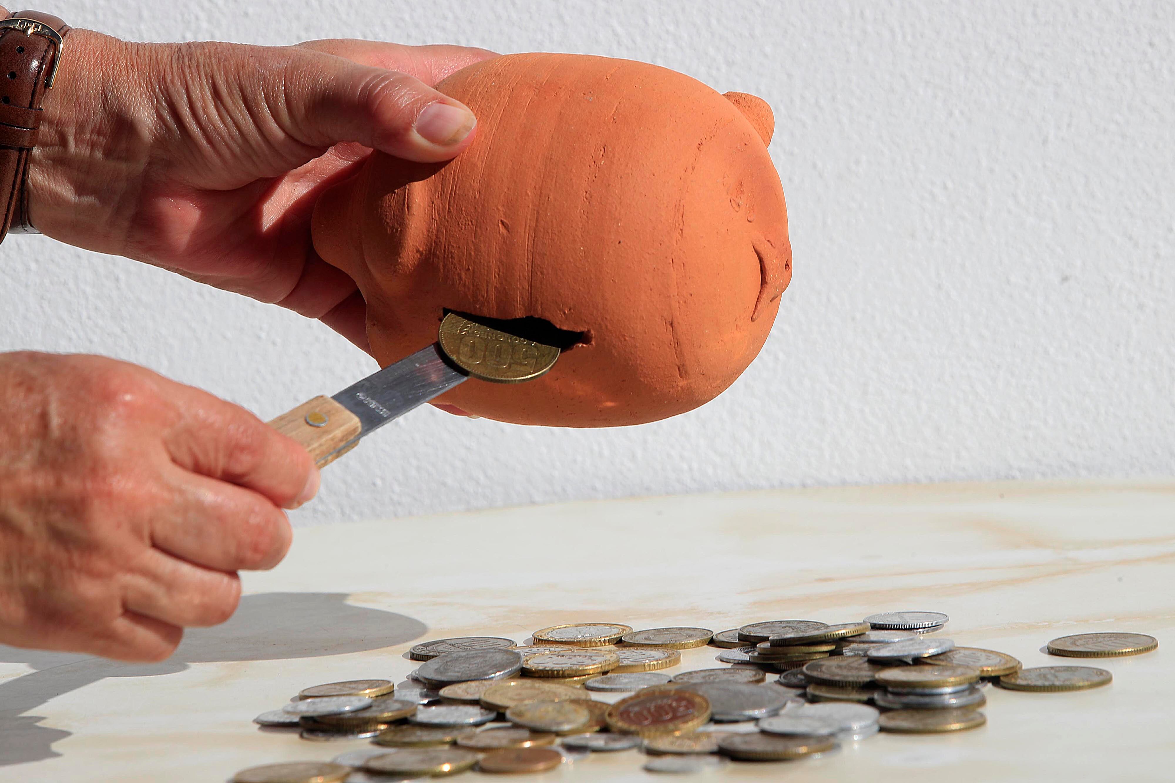 Una persona saca con ayuda de un cuchillo monedas de un alcancía.