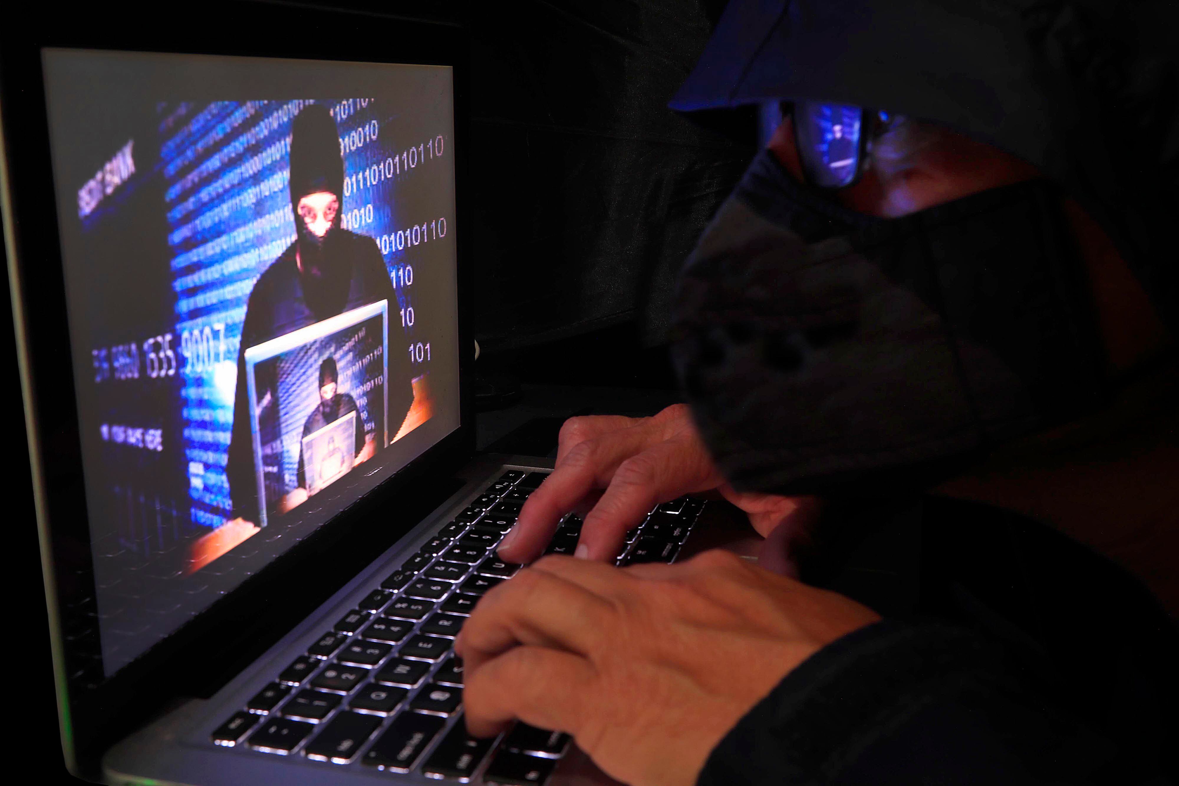 Primer plano de un hombre con capucha utilizando una computadora portátil, representando un ciberataque o actividad de hacking.