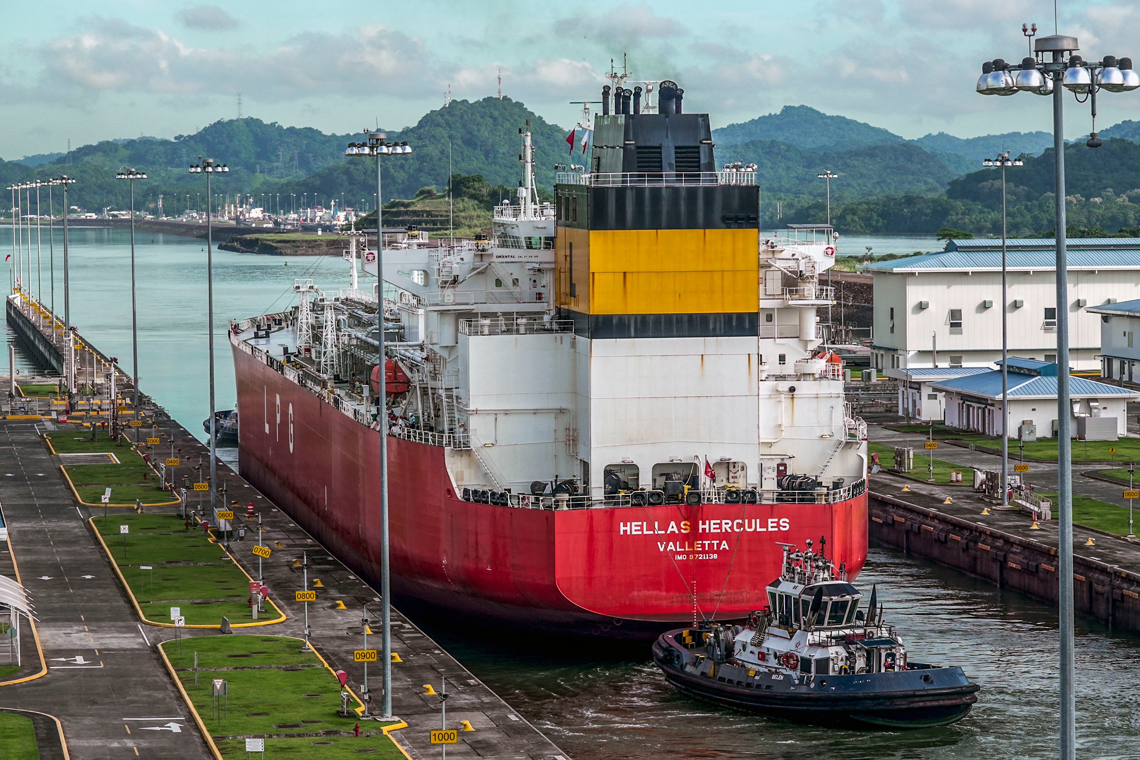 Un buque de transporte de gas licuado (LPG), identificado como Hellas Hercules, cruzando las esclusas de Agua Clara en el Canal de Panamá, rodeado de paisajes verdes y embarcaciones de apoyo.