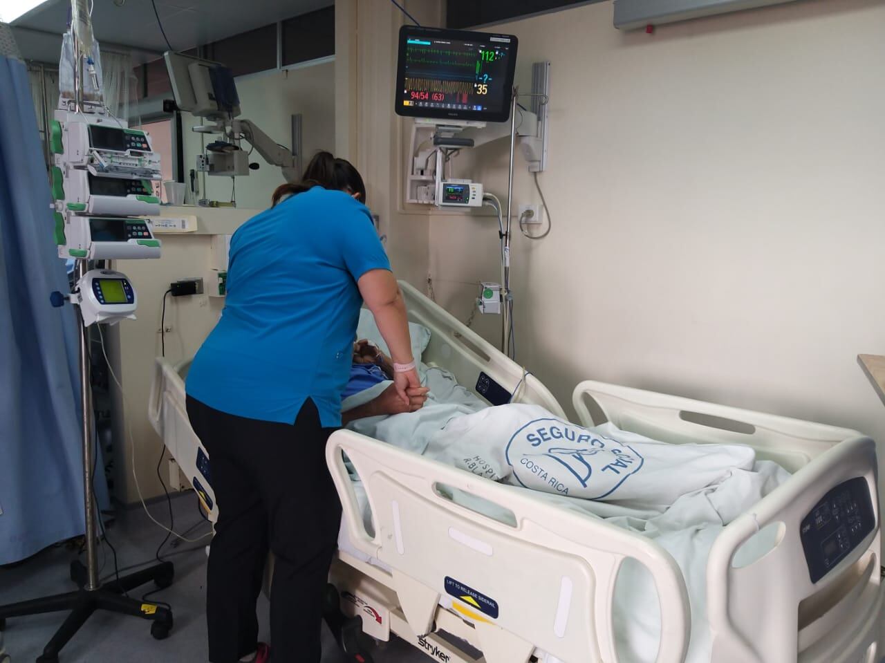 Enfermera atendiendo a un paciente adulto mayor en una cama hospitalaria del Hospital Blanco Cervantes, especializado en geriatría.