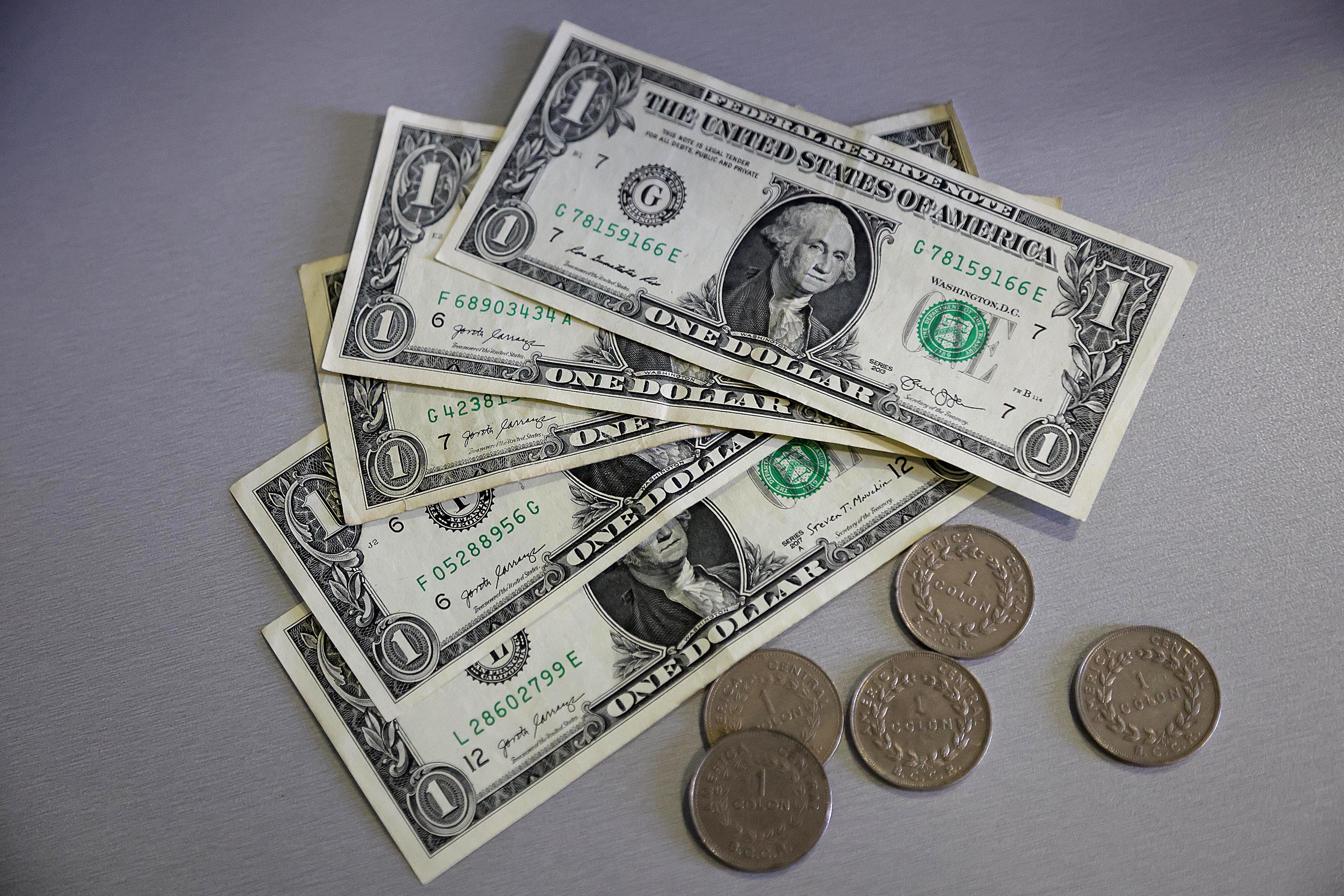 Billetes de un dólar y monedas sobre una superficie gris, representando el tipo de cambio en Costa Rica.