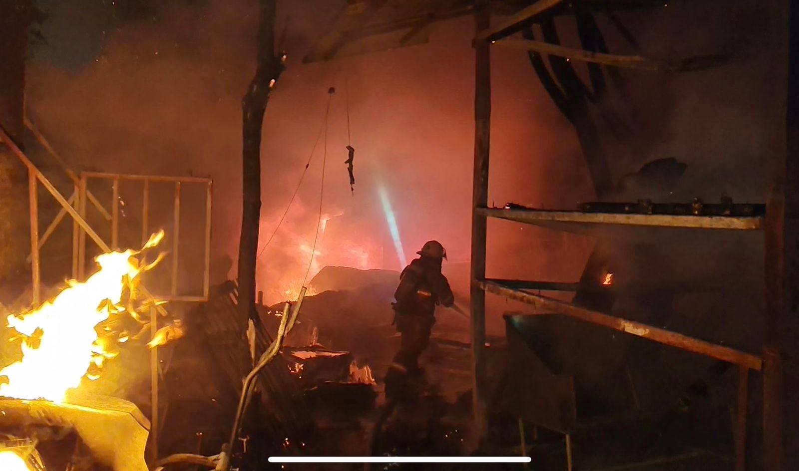Un incendio en la noche, un bombero tratando de apagarlo.
