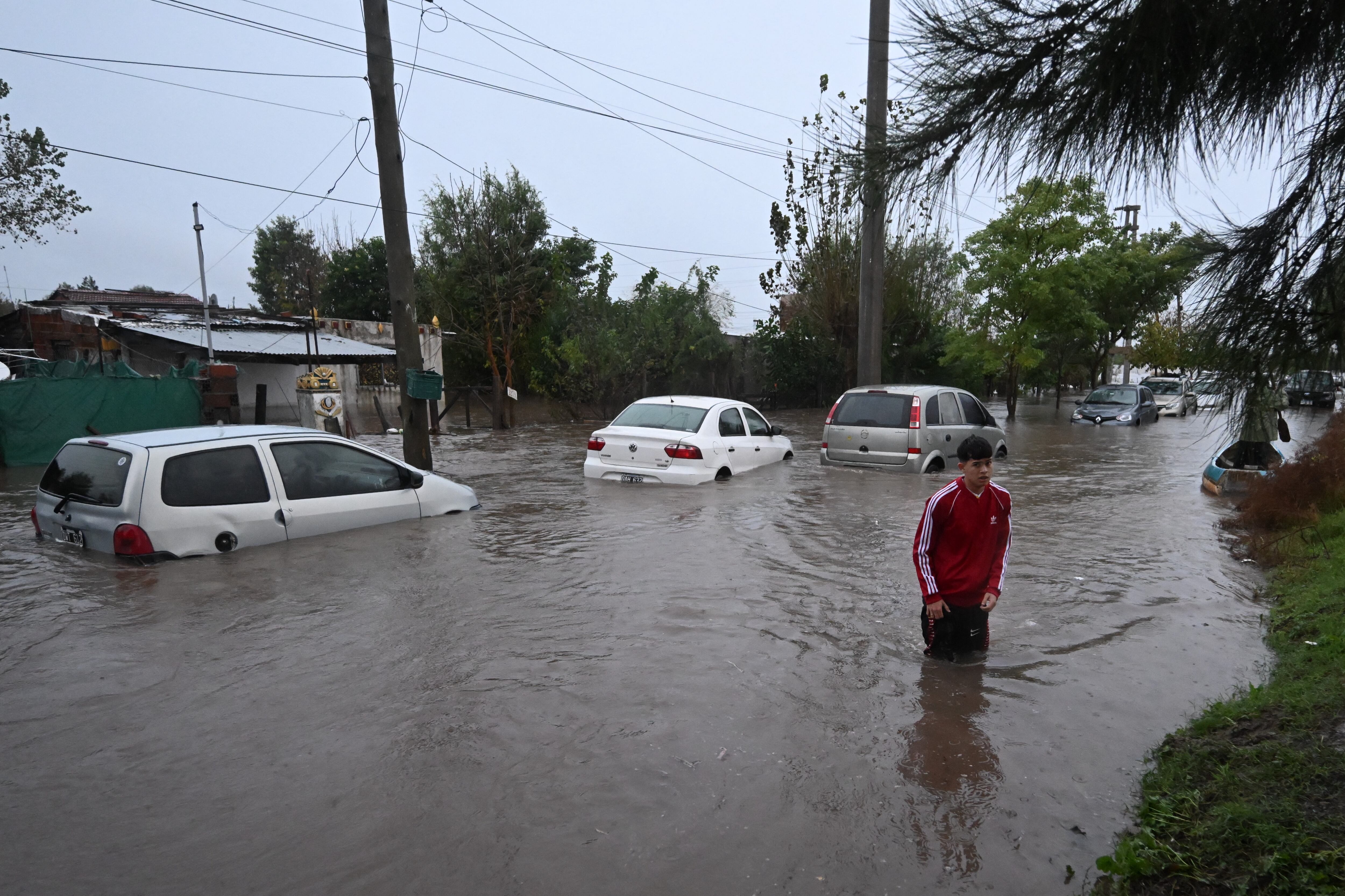 Un hombre camina por las calles inundadas de Buenos Aires. Detrás, se ven varios vehículos cuyos neumáticos están cubiertos por el agua.