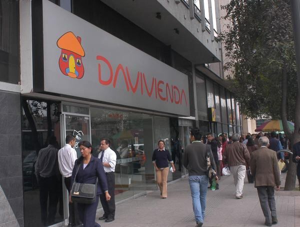 Vista frontal de una sucursal de Davivienda, con peatones transitando frente al edificio en una calle urbana.