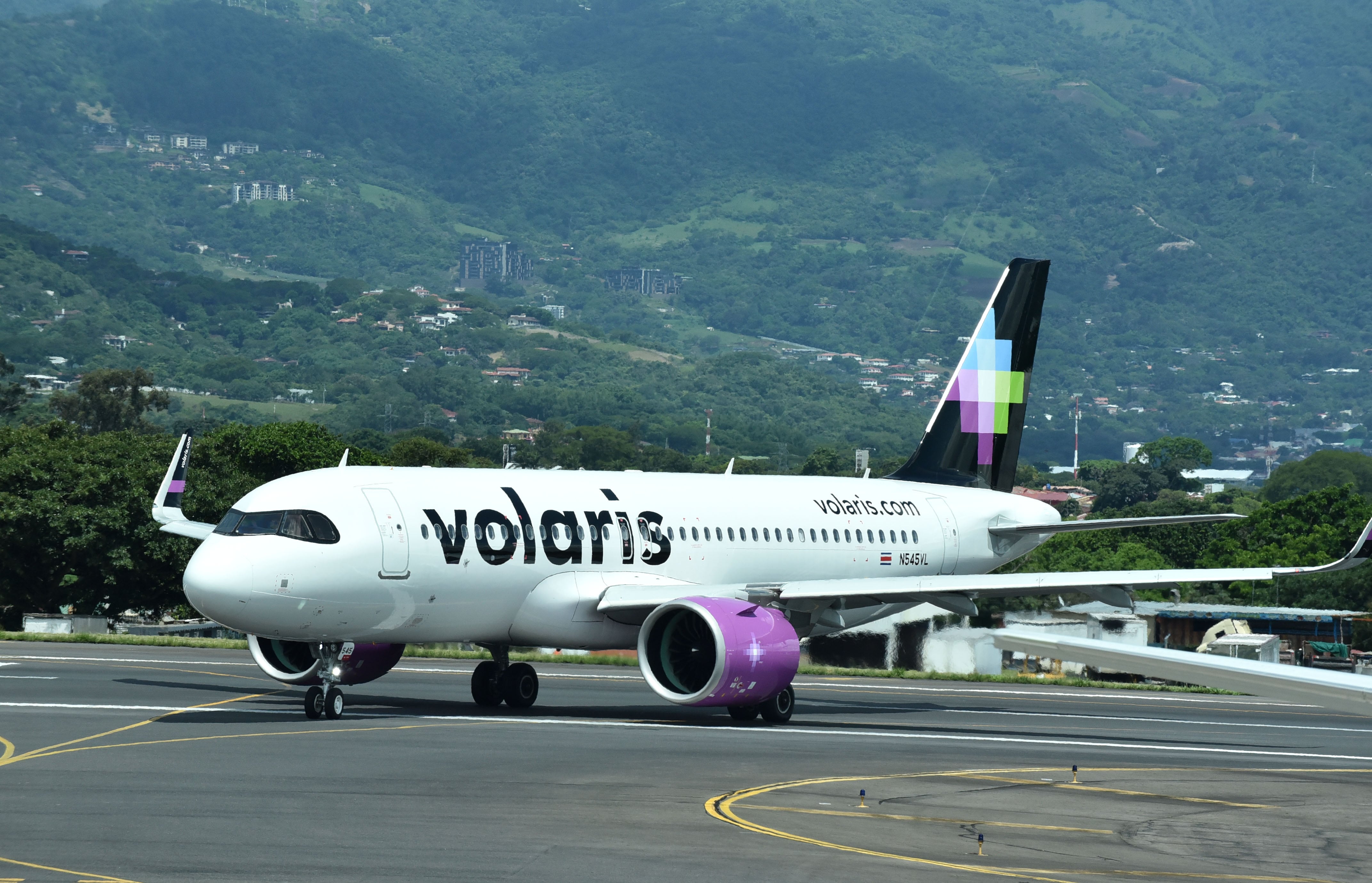 Avión de Volaris en el Aeropuerto Juan Santamaría, Costa Rica, con montañas verdes al fondo. La aerolínea anunció nuevas rutas a Tulum, Miami y Orlando.