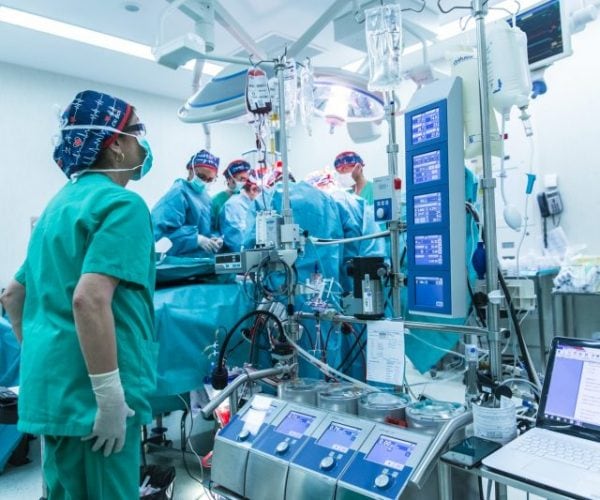 Quirófano de un hospital. Personal vestido de verde para operar. Máquinas de anestesia y para tomar signos a paciente en cirugía.