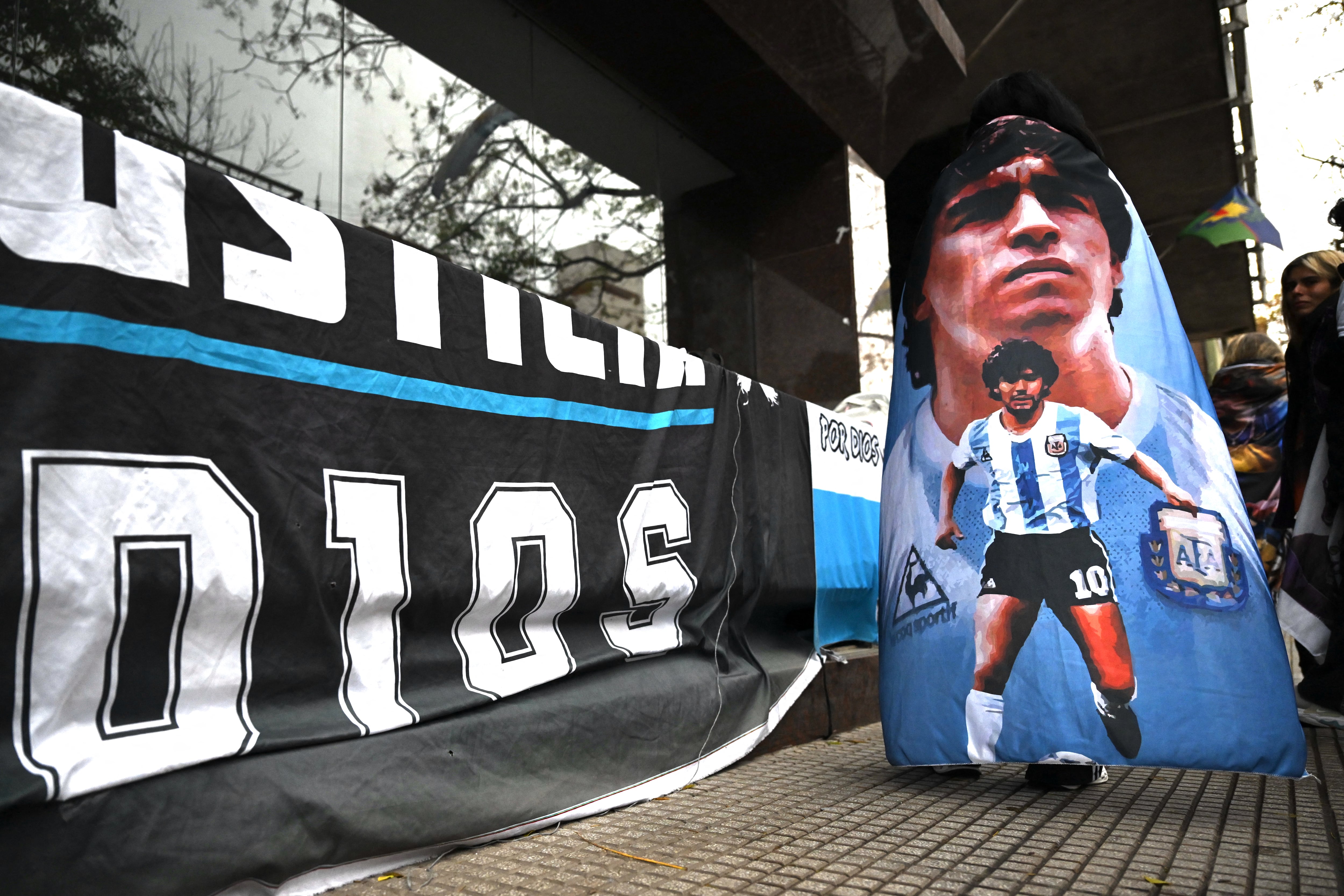 Un aficionado se cubrió con esta bandera y mostró una manta en las afueras del jucio por la muerte de Diego Armando Maradona, en la localidad argentina de San Isidro.