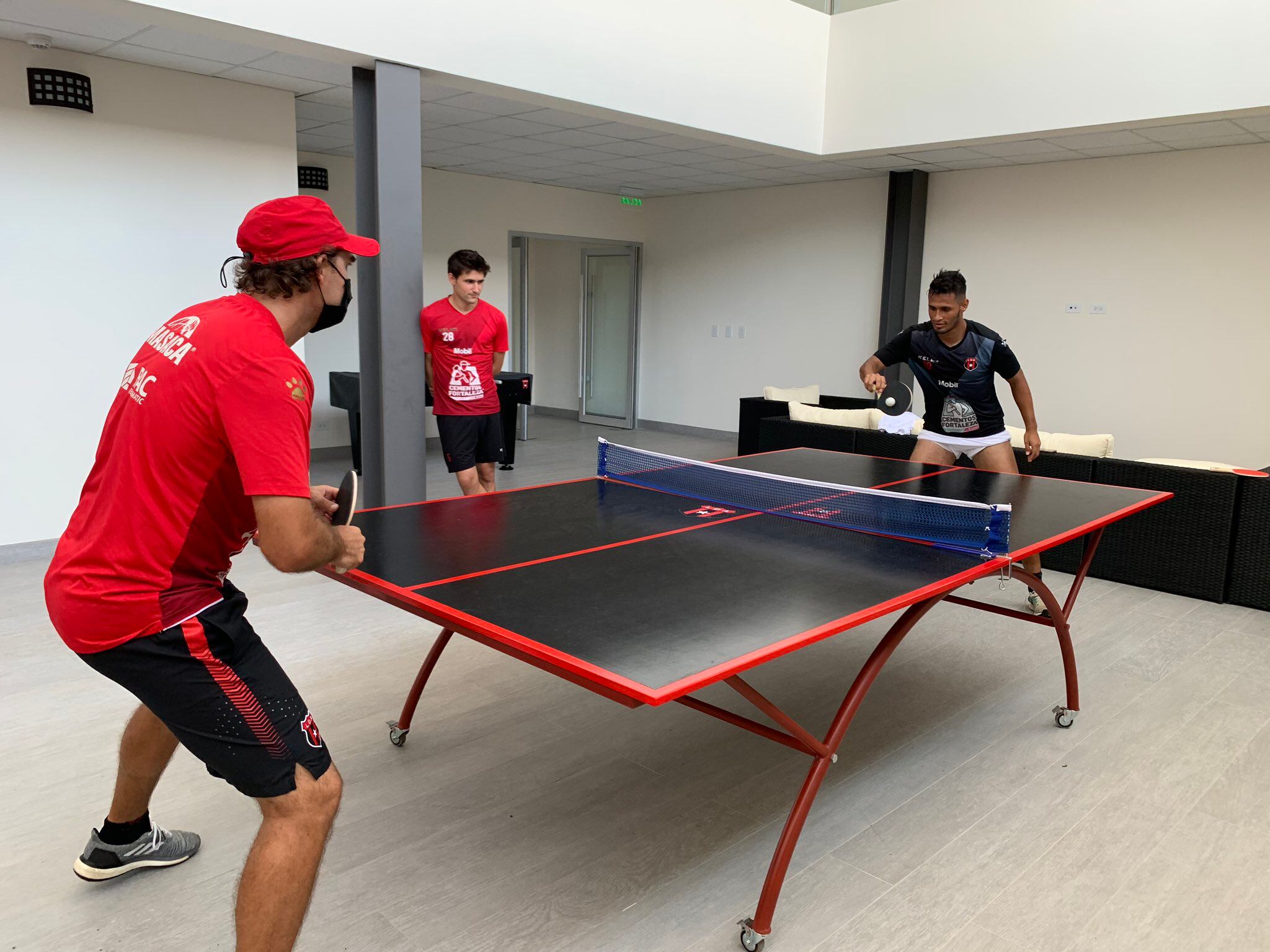 Andrés Carevic y Alex López afrontan un partido de ping pong en el CAR, con Sergi Rounge como testigo. Fotografía: Prensa Alajuelense
