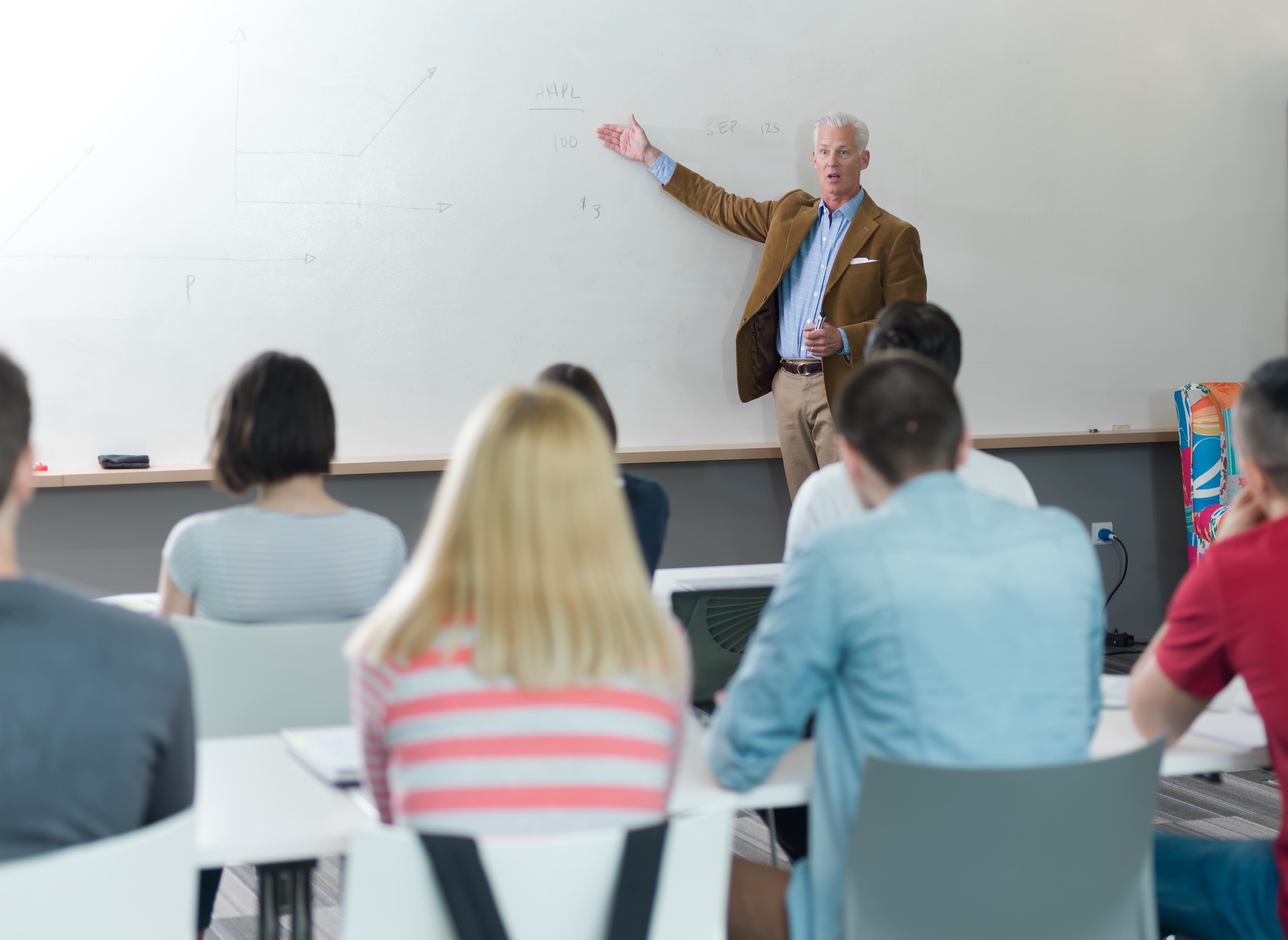 Profesor de universidad dando clases, estudiantes de espaldas.