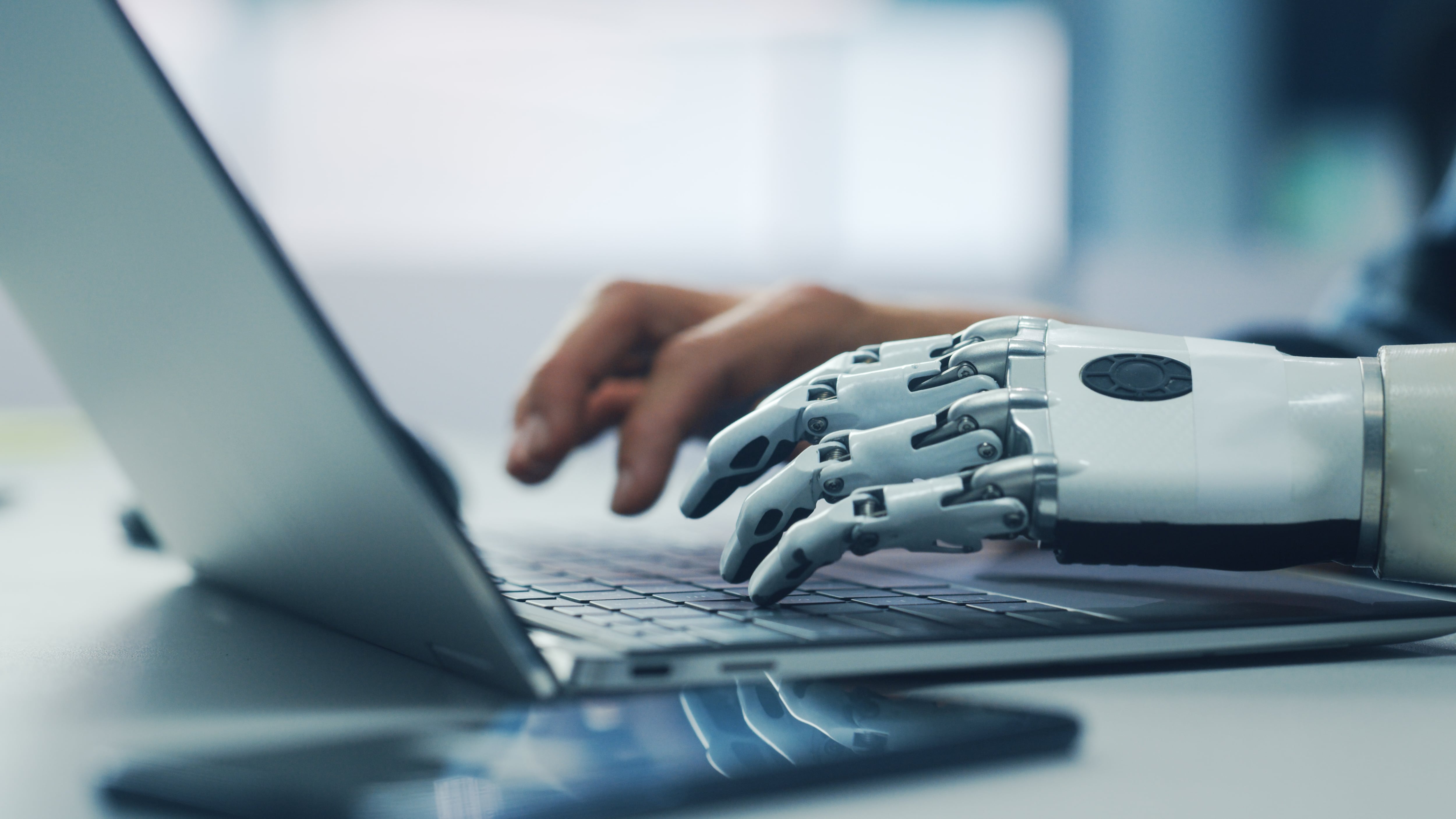 Inteligencia artificial en el trabajo. Reforma laboral escrita por la IA. Dos manos, una humana y otra de un robot, escriben sobre el mismo teclado de una laptop