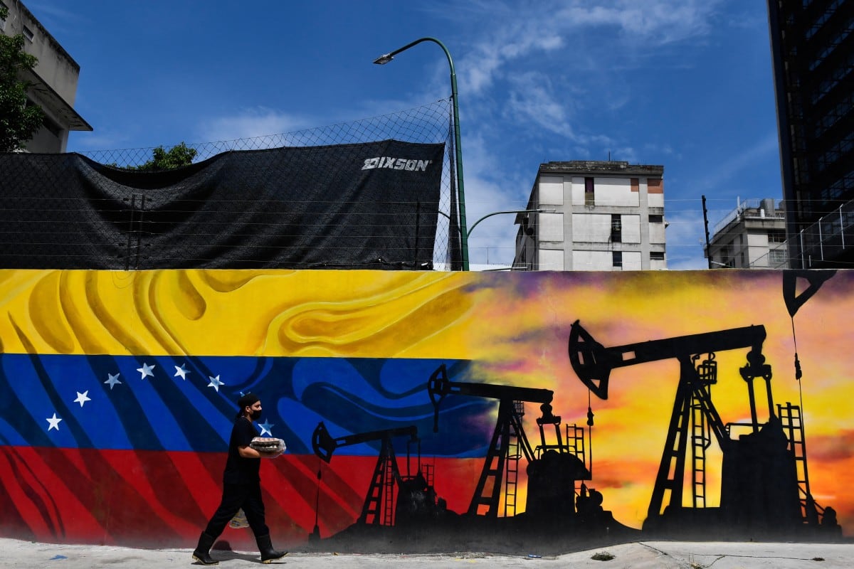 Un hombre que lleva una mascarilla camina frente a un mural que representa una bomba petrolera y la bandera venezolana en una calle de Caracas, el 26 de mayo de 2022.