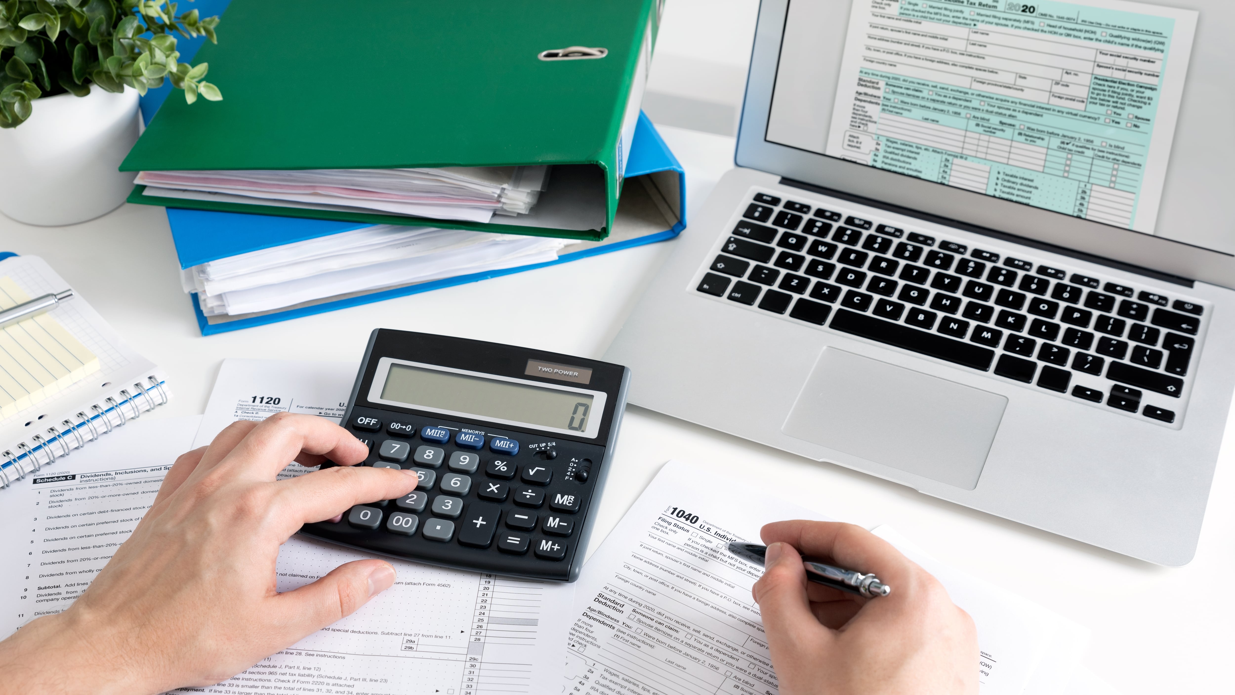 Fotografía ilustrativa de una persona usando una calculadora y completando formularios de impuestos en un escritorio con una computadora portátil y carpetas con documentos, representando la digitalización del sistema tributario en Costa Rica.