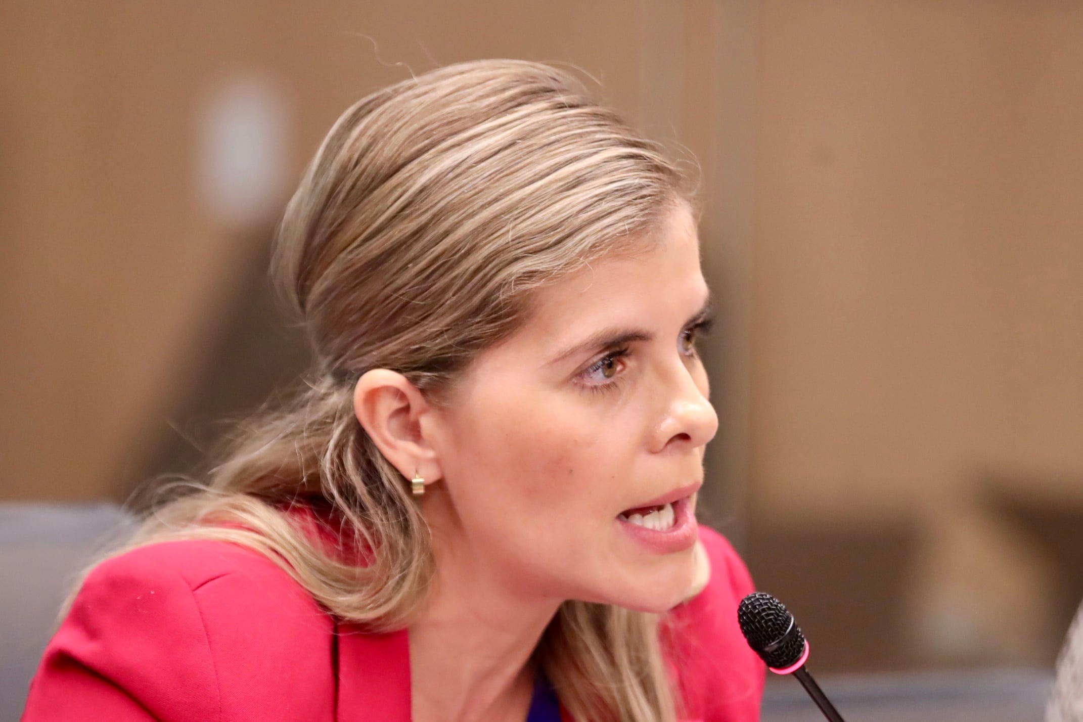 Fotografía de Laura Fernández, ministra de la Presidencia de Costa Rica,  frente a un micrófoto. Lleva un traje formal rojo.