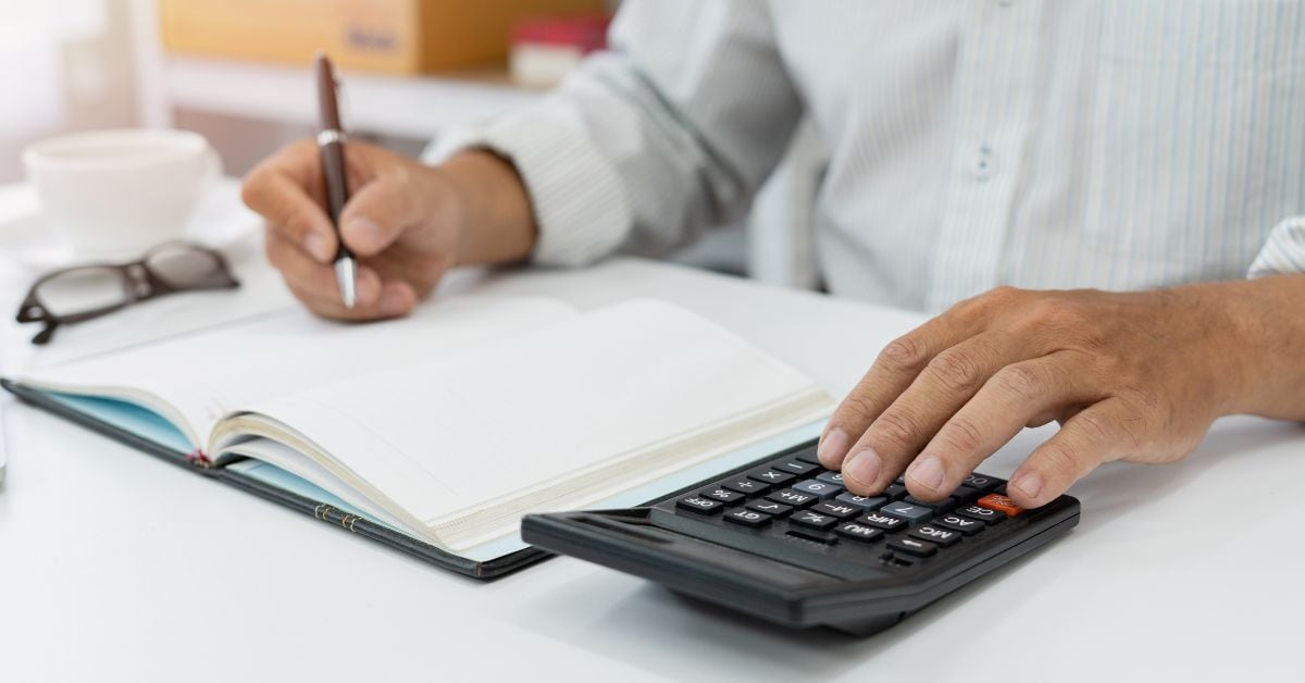 En la imagen, alguien anotando en una libreta con una calculadora