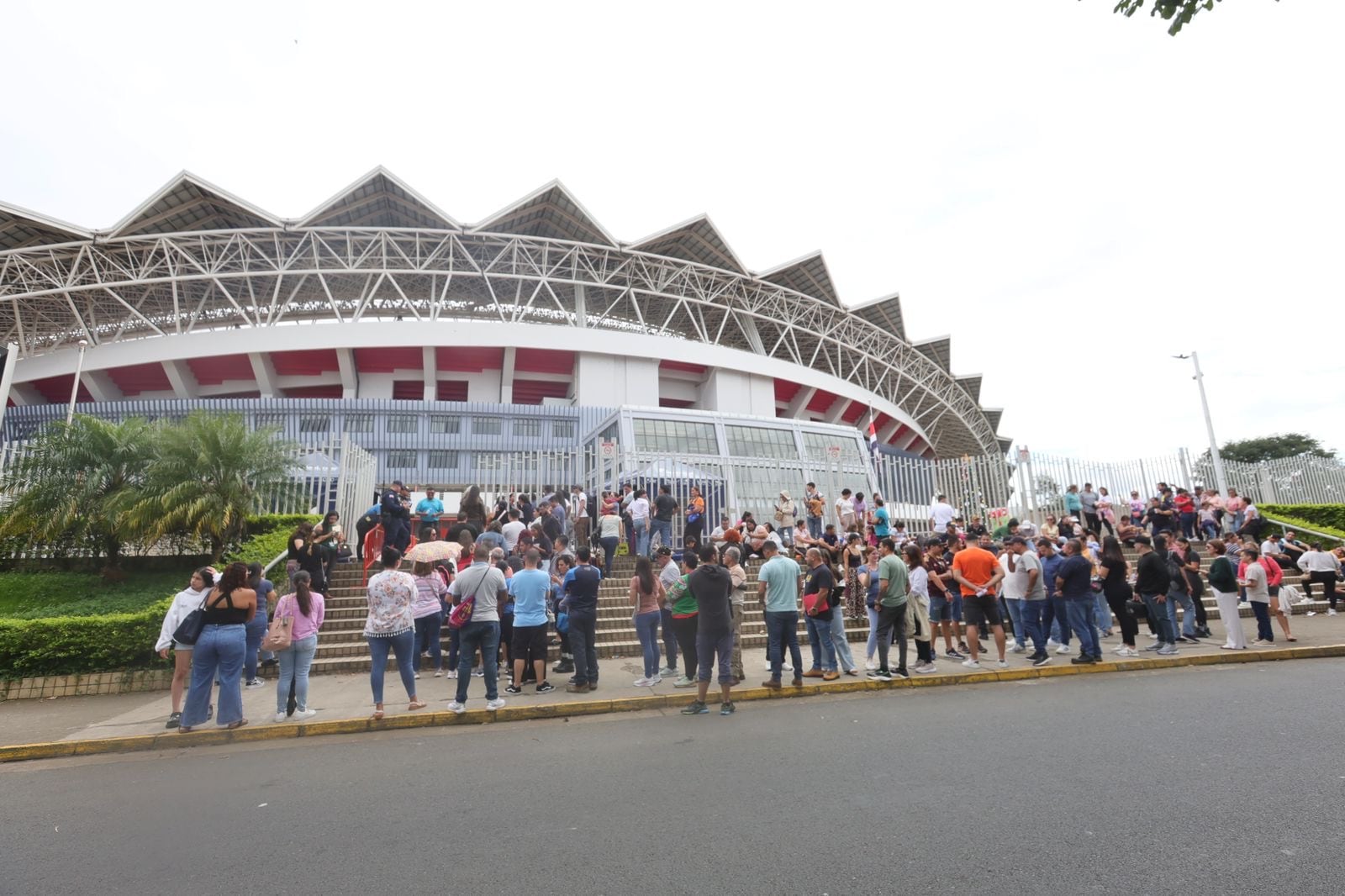 Decenas de personas en fila en una acera frente al estadio nacional, en La Sabana.