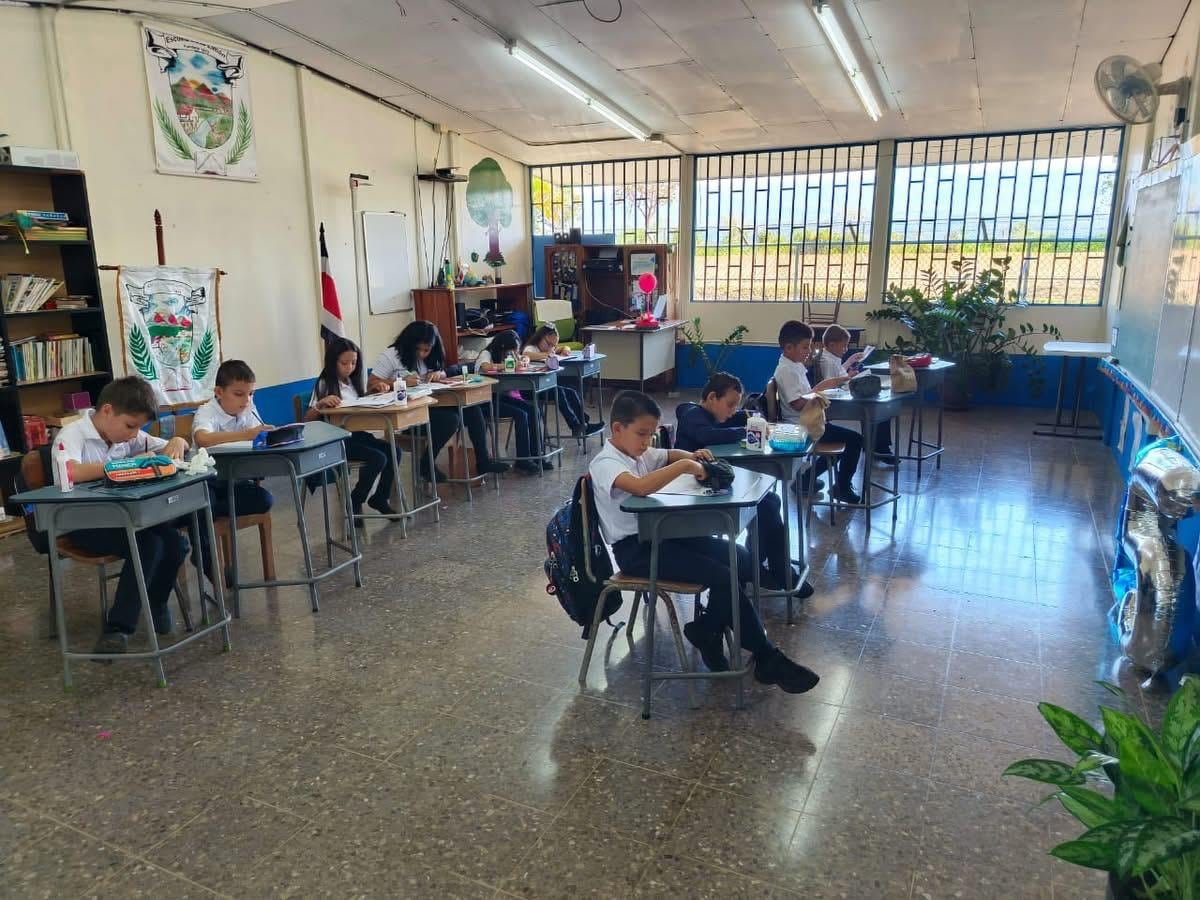 Estudiantes sentados en sus pupitres en un aula con un ventanal al fondo.