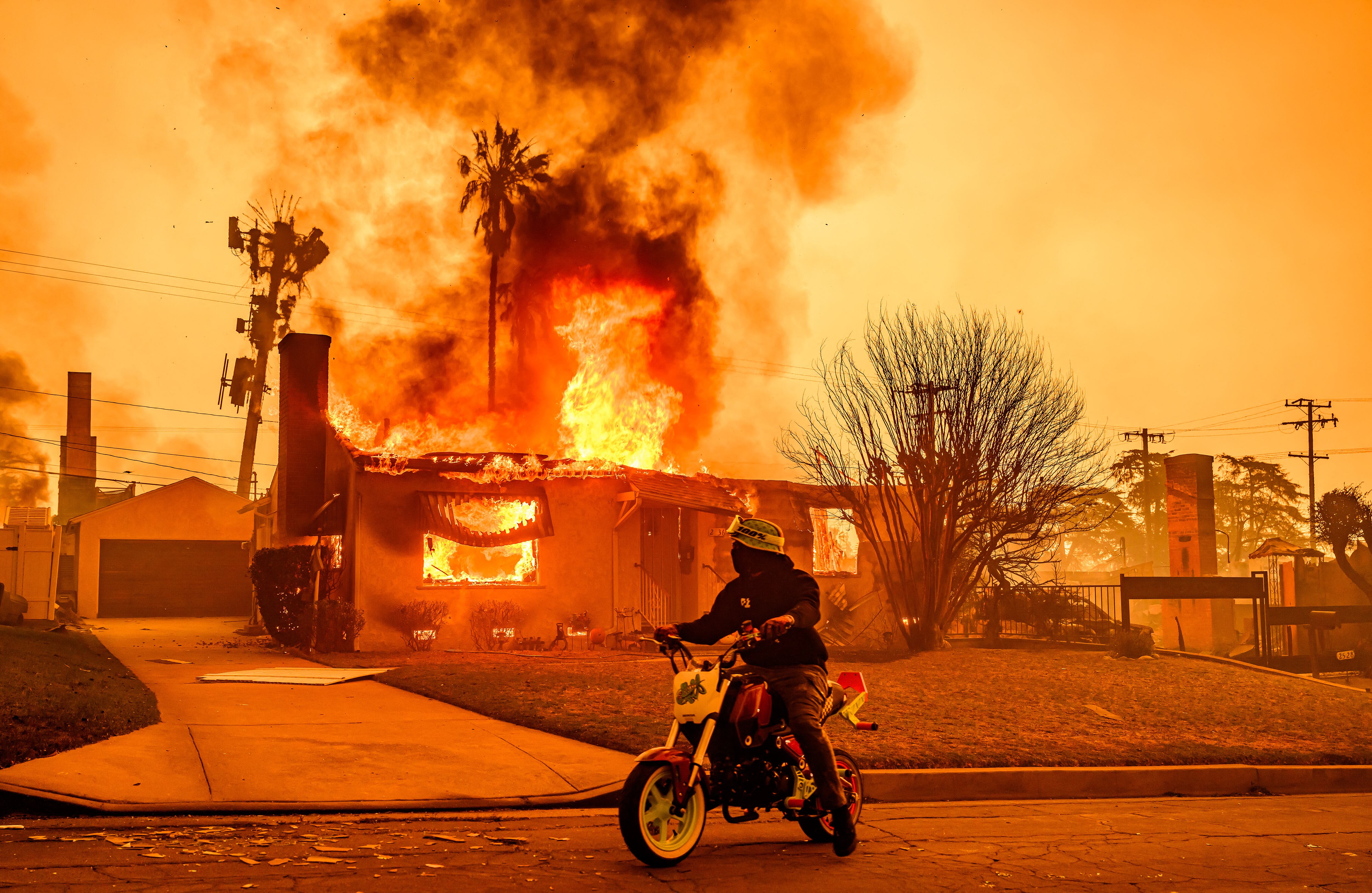 Un motociclista se detiene para mirar una casa en llamas durante el incendio de Eaton en el área de Altadena del condado de Los Ángeles, California