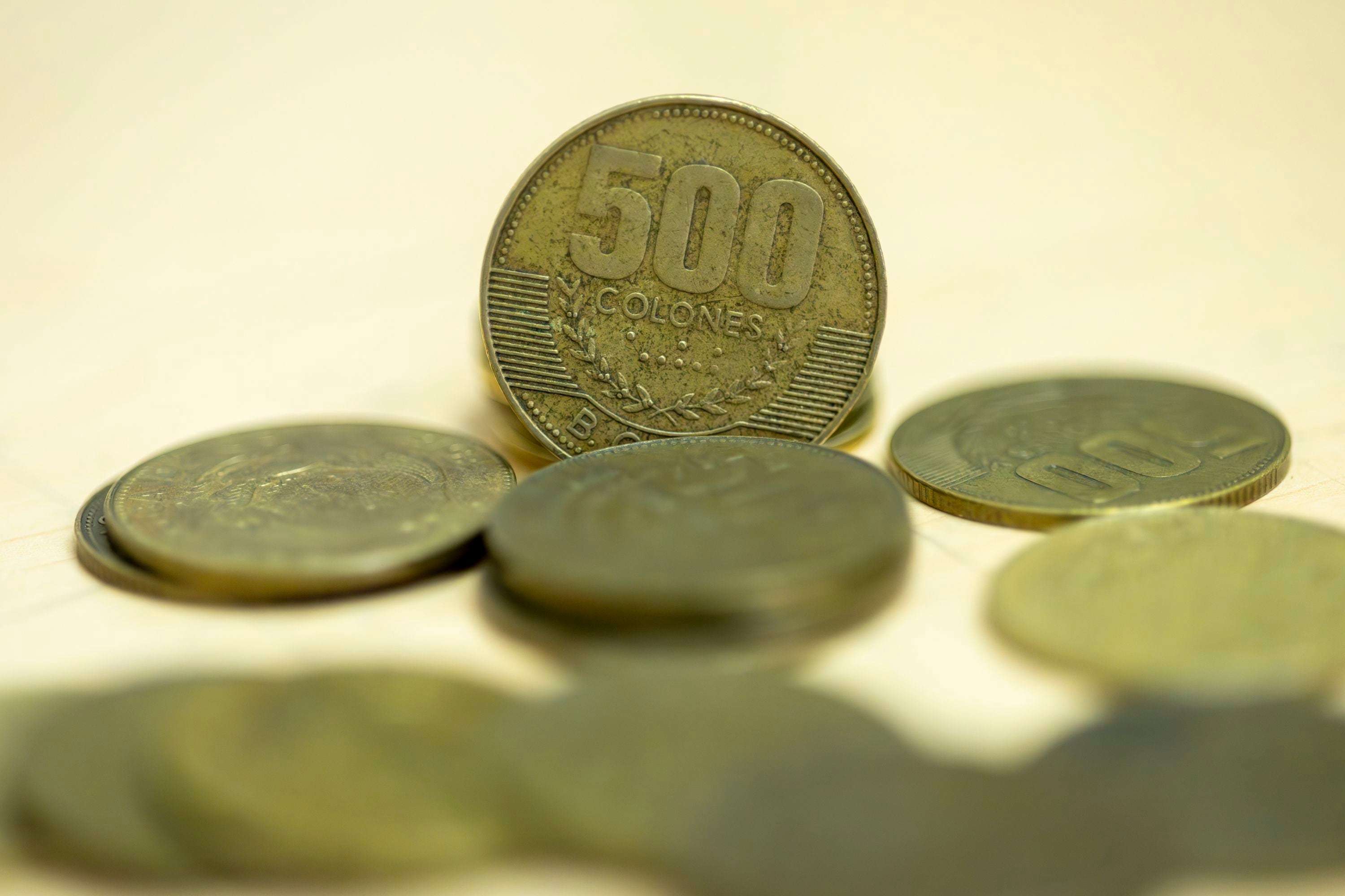 Moneda dorada de ¢500 de Costa Rica en primer plano, rodeada de otras monedas, en referencia a su retiro de circulación y sustitución por una nueva versión bimetálica.