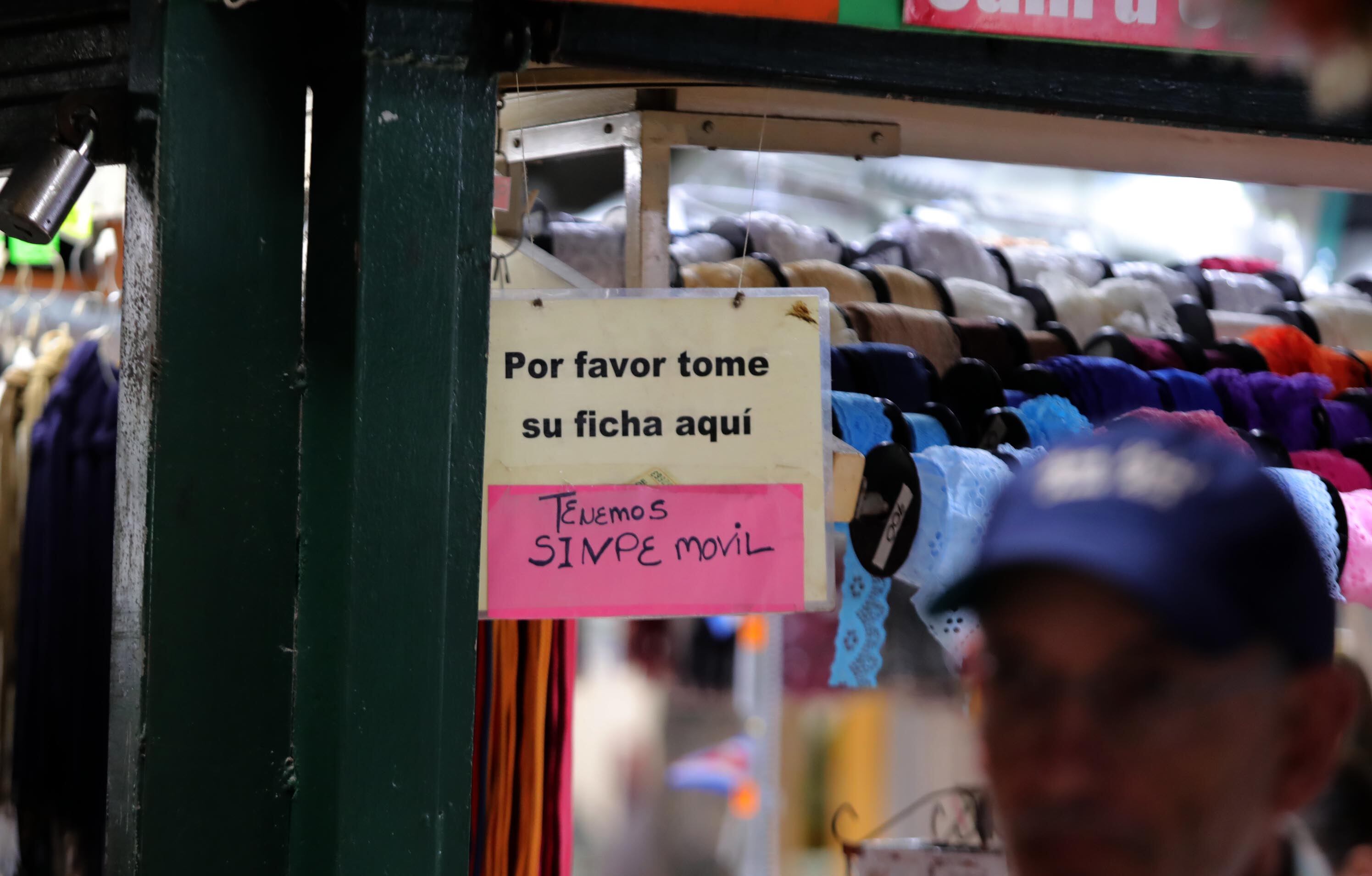 Aviso en un comercio costarricense que indica la disponibilidad de pagos mediante Sinpe Móvil, con fondo de mostrador de cintas y telas.