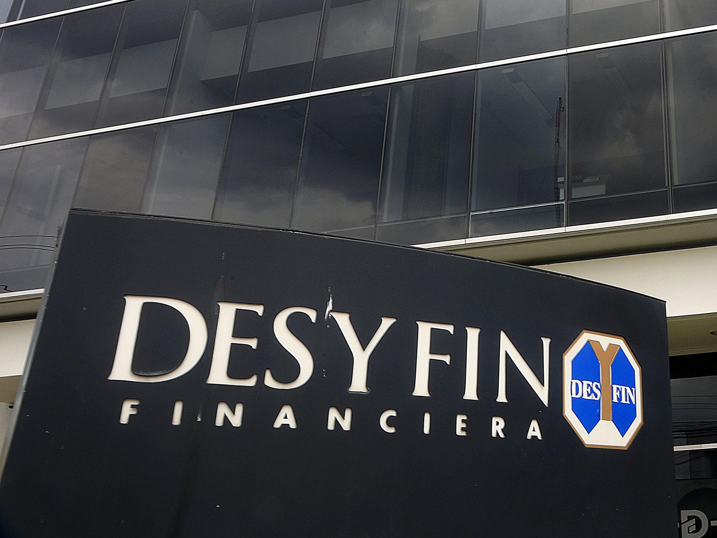 Fachada de la sede de Financiera Desyfin en Costa Rica, con un rótulo negro con el nombre de la empresa en letras blancas. El edificio de vidrio se refleja en el fondo.