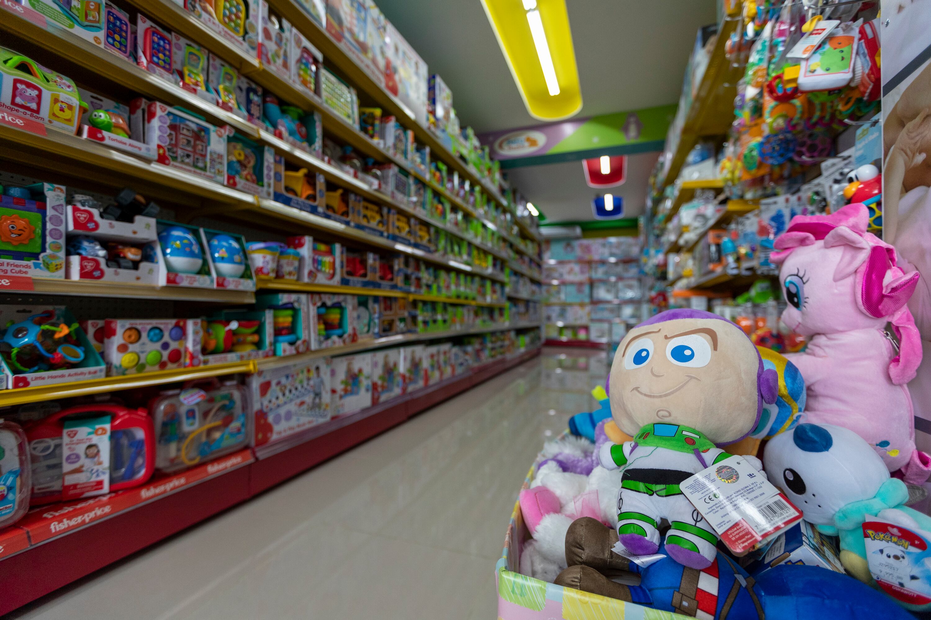 Pasillo de tienda con estantes llenos de juguetes de colores, incluyendo peluches y juegos educativos, recomendados para niños de diferentes edades durante la Navidad.