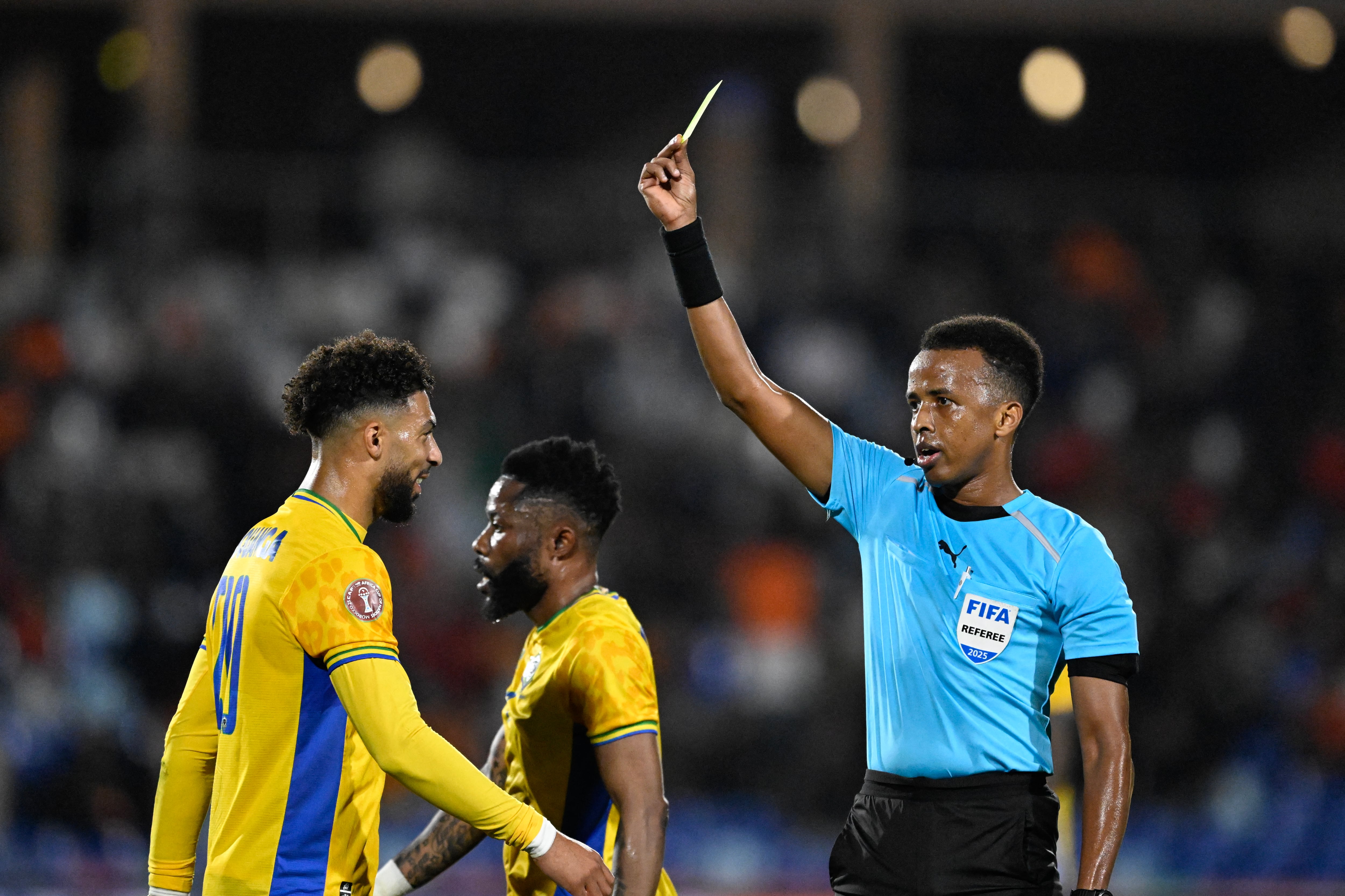 El delantero de Gabón Denis Bouanga (#20) recibe una tarjeta amarilla del árbitro somalí Omar Abdulkadir Artan durante el partido del Grupo F de la Copa Africana de Naciones (CAN) entre Gabón y Costa de Marfil, disputado en el Gran Estadio de Marrakech el 31 de diciembre de 2025. (Foto: Khaled Desouki / AFP).