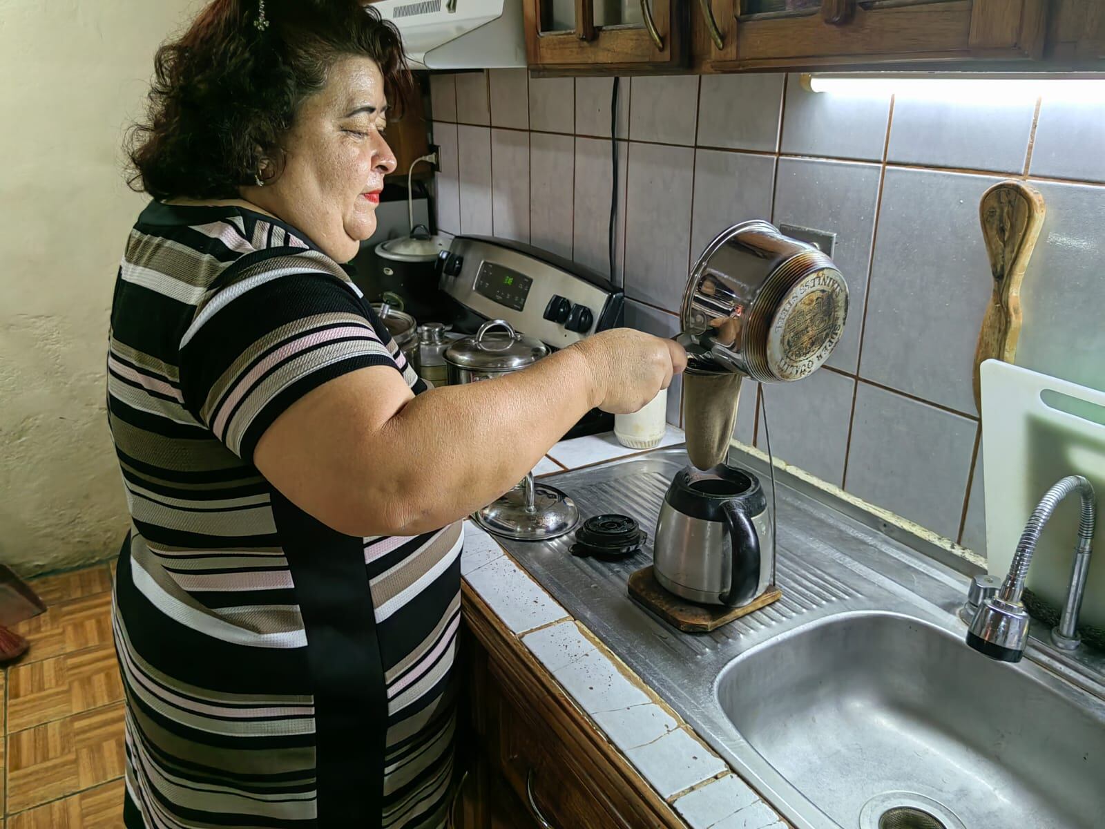 El ministro de vivienda Fernando Zumbado Jiménez con un oso de peluche, tras pasar la noche en un tugurio de Lomas del Río, Pavas, el 29 de mayo del 2007. En la foto doña Ingrid Ríos Álvarez chorrea cafecito en el 2022, en su casa de Pavas.
