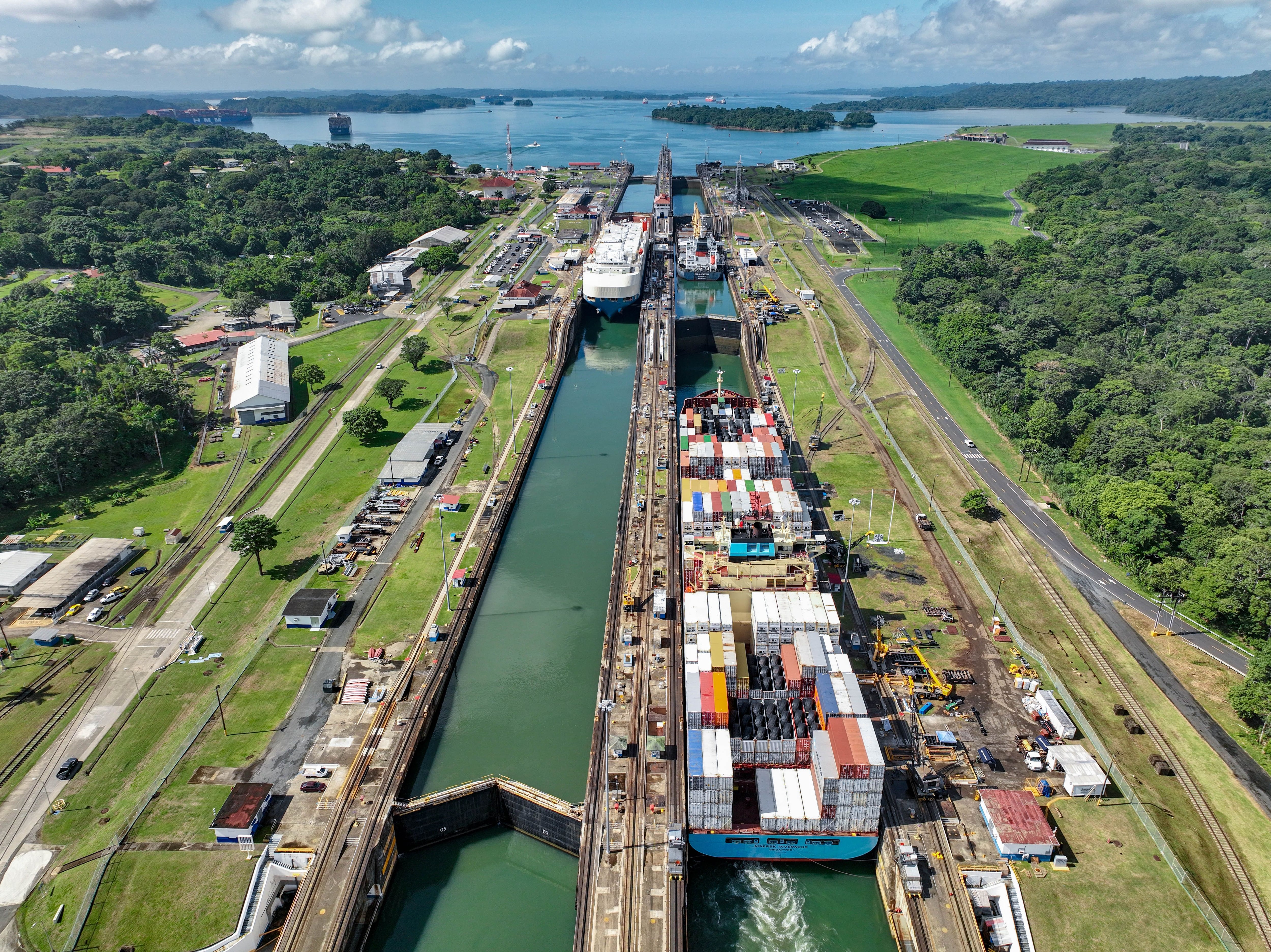 Vista aérea del canal de Panamá con barcos transitando por las esclusas, rodeado de vegetación y áreas de operación logística.