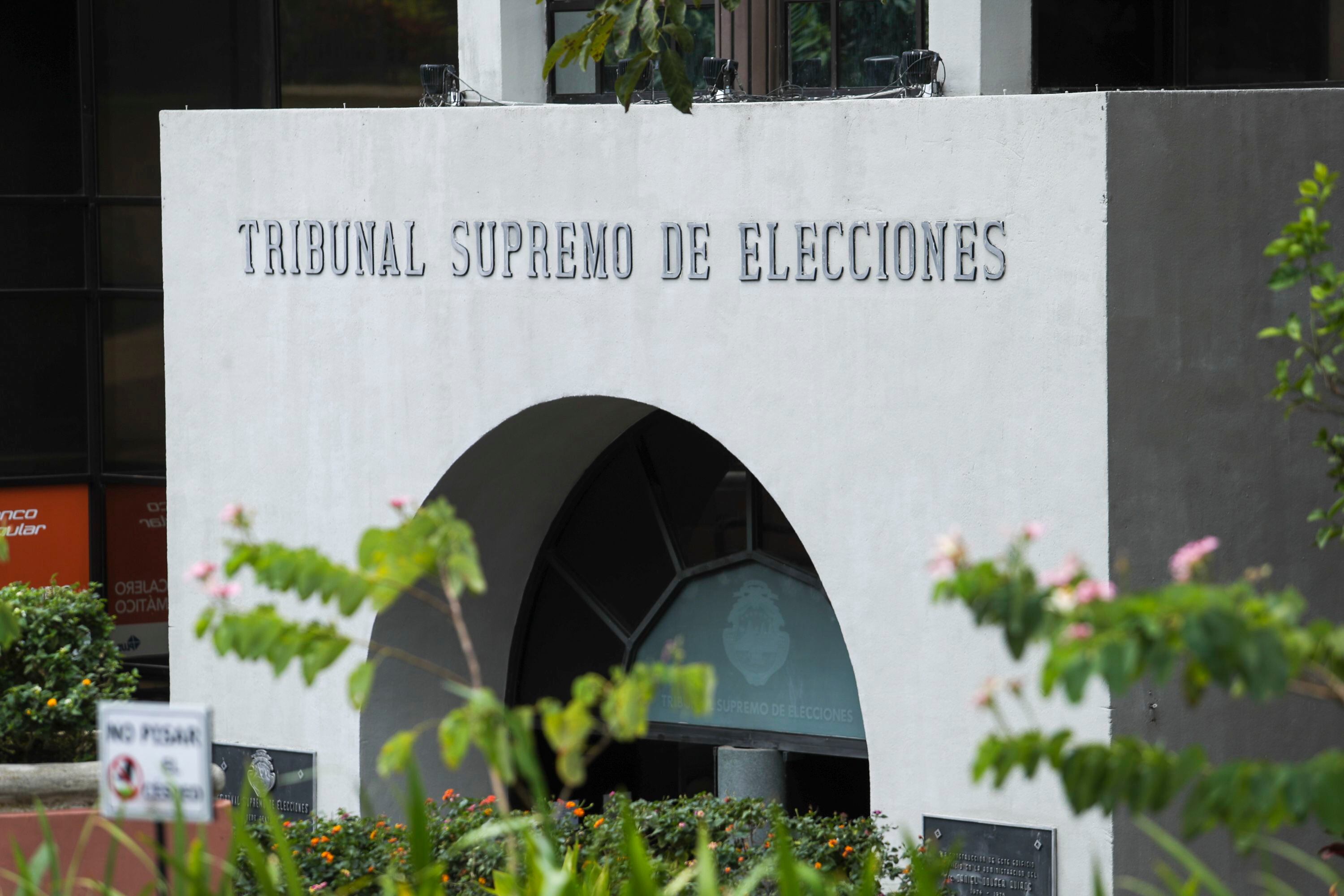 Fachada del Tribunal Supremo de Elecciones de Costa Rica, edificio blanco con un arco central rodeado de plantas.