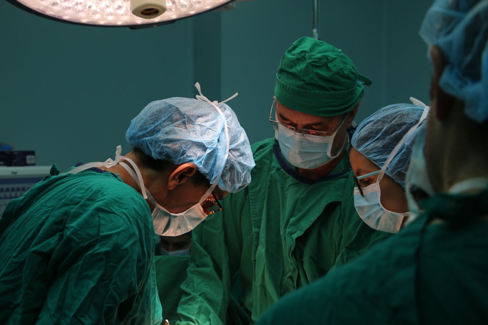 Quirófano oscuro, cuatro personas vestidas de verde con mascarillas. La poca luz que hay viene del techo, es una lámpara quirúrgica.