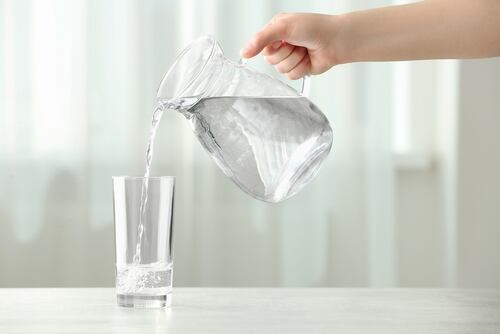 Una mano vierte agua de una jarra en un vaso, representando la importancia de la hidratación para la salud
