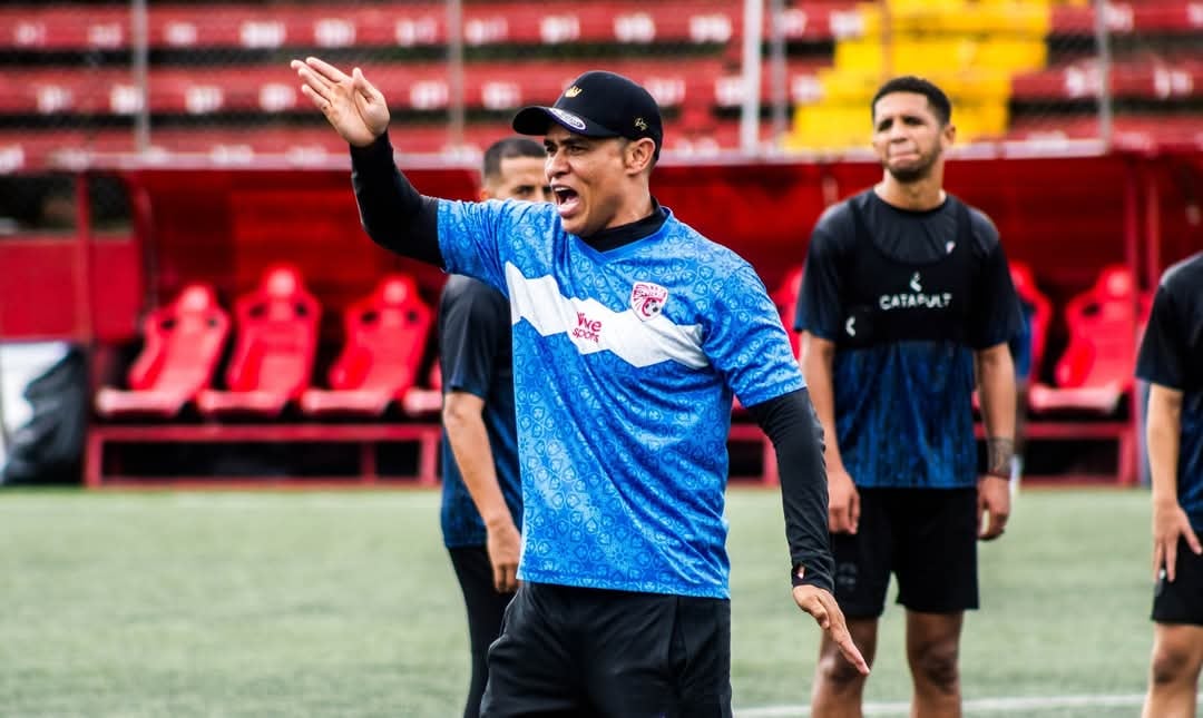 Wálter Paté Centeno, técnico del Santos de Guápiles, dirige una sesión de entrenamiento en el estadio, con jugadores al fondo.