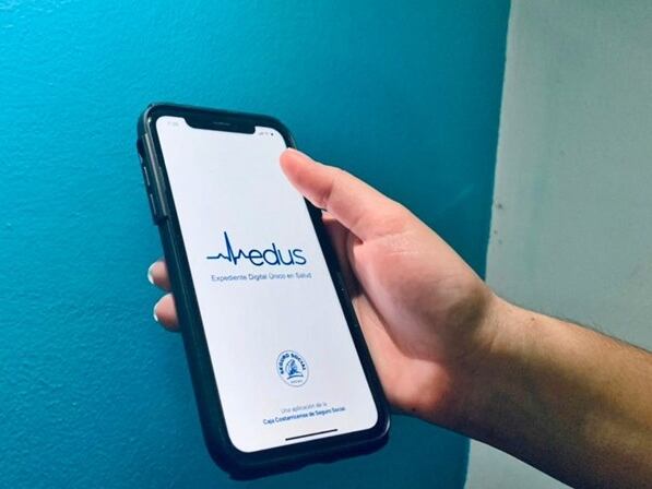 Mano sostiene un teléfono celular donde se ve la portada de la aplicación EDUS