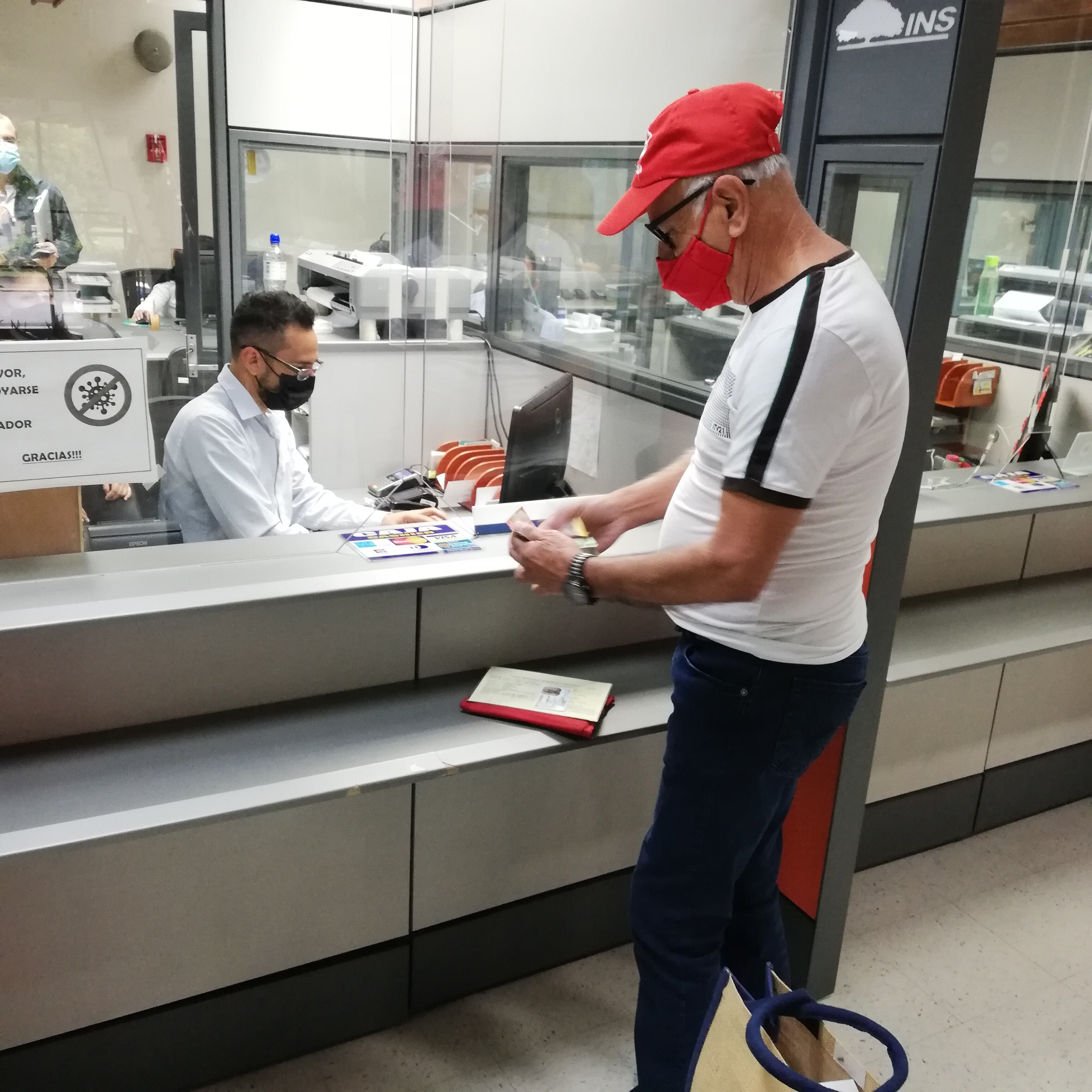 Don Carlos Chacón Alvarado, pensionado y de 73 años, cumplió por 13 años consecutivos su compromiso de ser el primer tico que paga el derecho de circulación 2022. En la foto el cajero del INS, Alejandro Molina, le recibe el pago del marchamo 2022 a don Carlos.